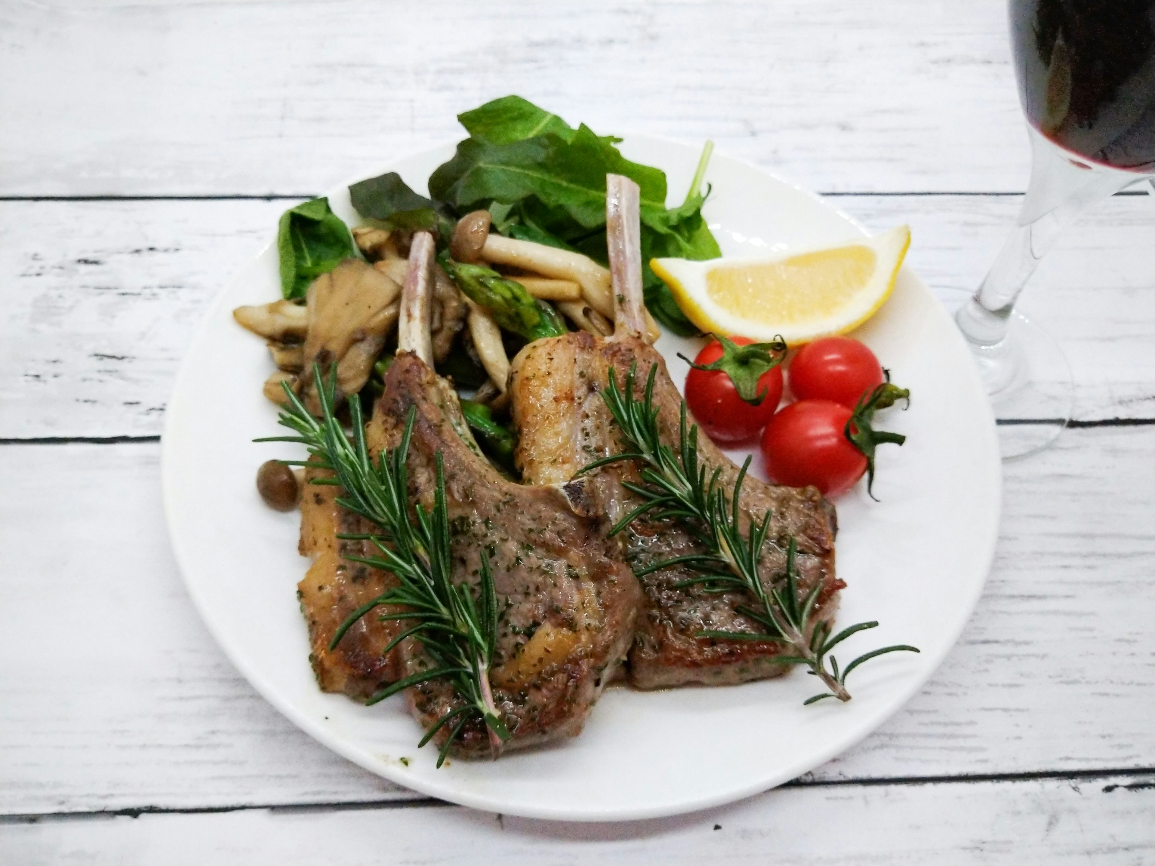 Costolette d'agnello arrosto servite con insalata pomodorini e fette di limone