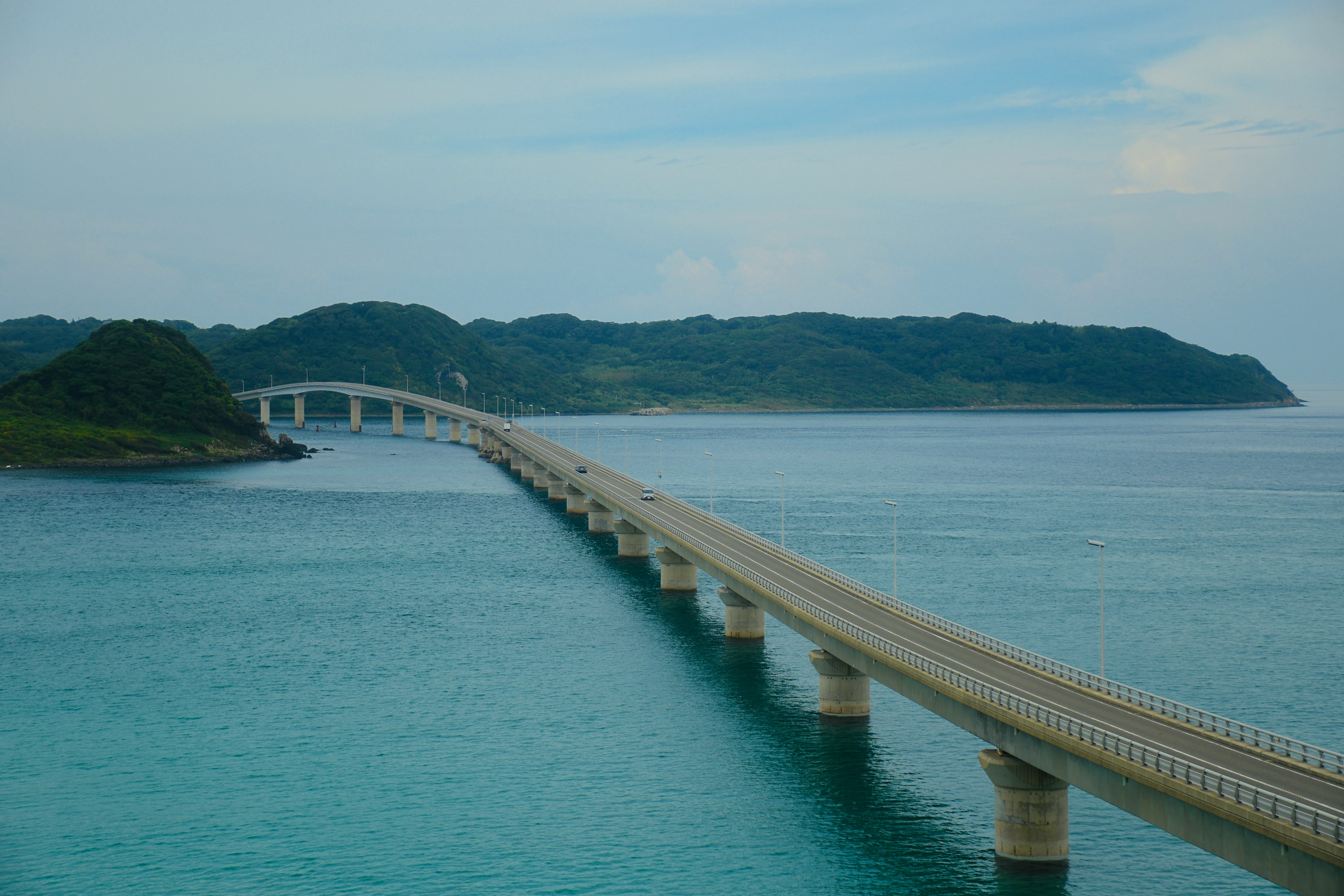 一座長橋橫跨藍色水面，通向綠色島嶼