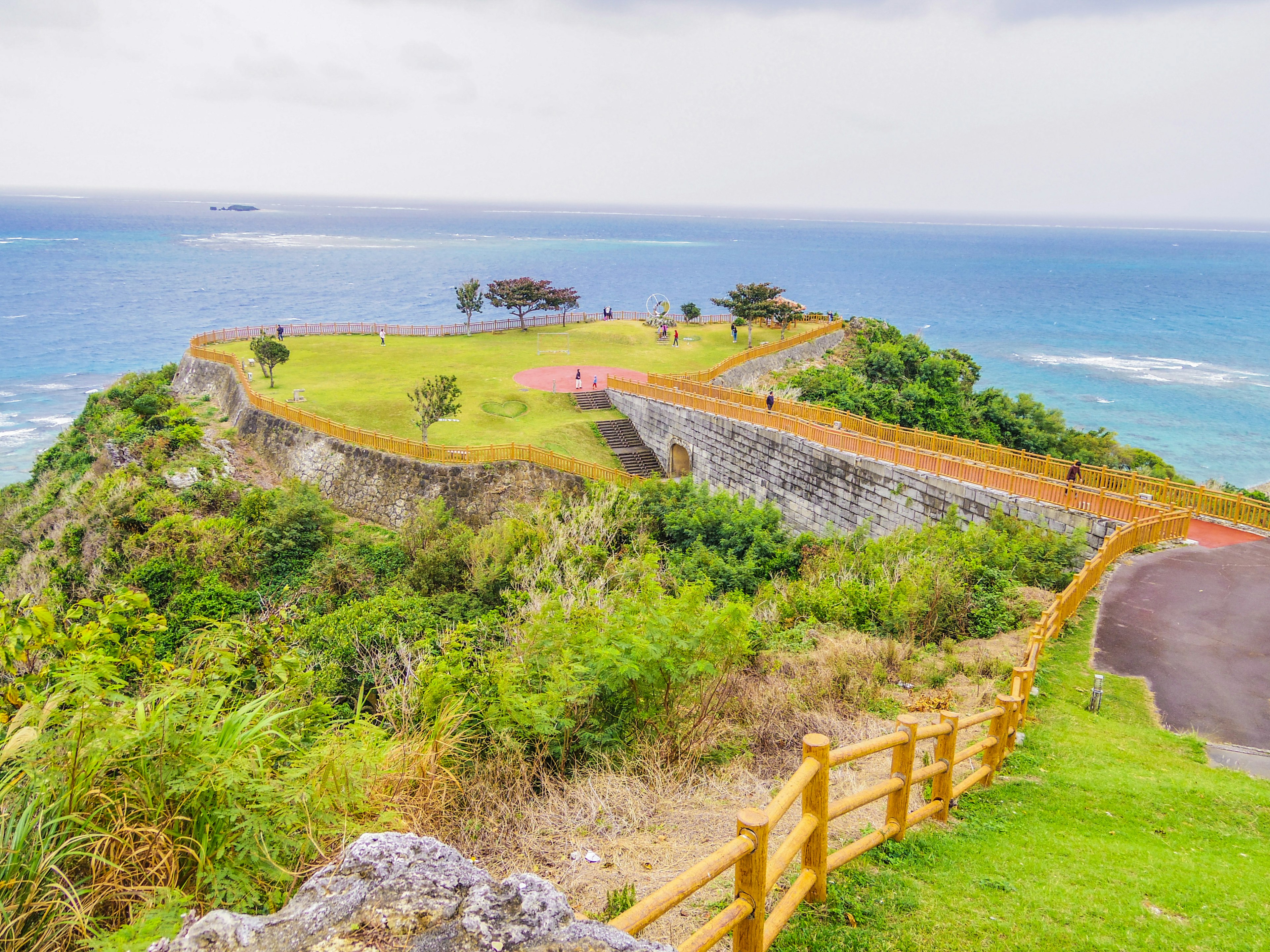 Vista escénica de un paisaje costero con colinas verdes y océano al fondo que incluye un parque y una cerca de madera