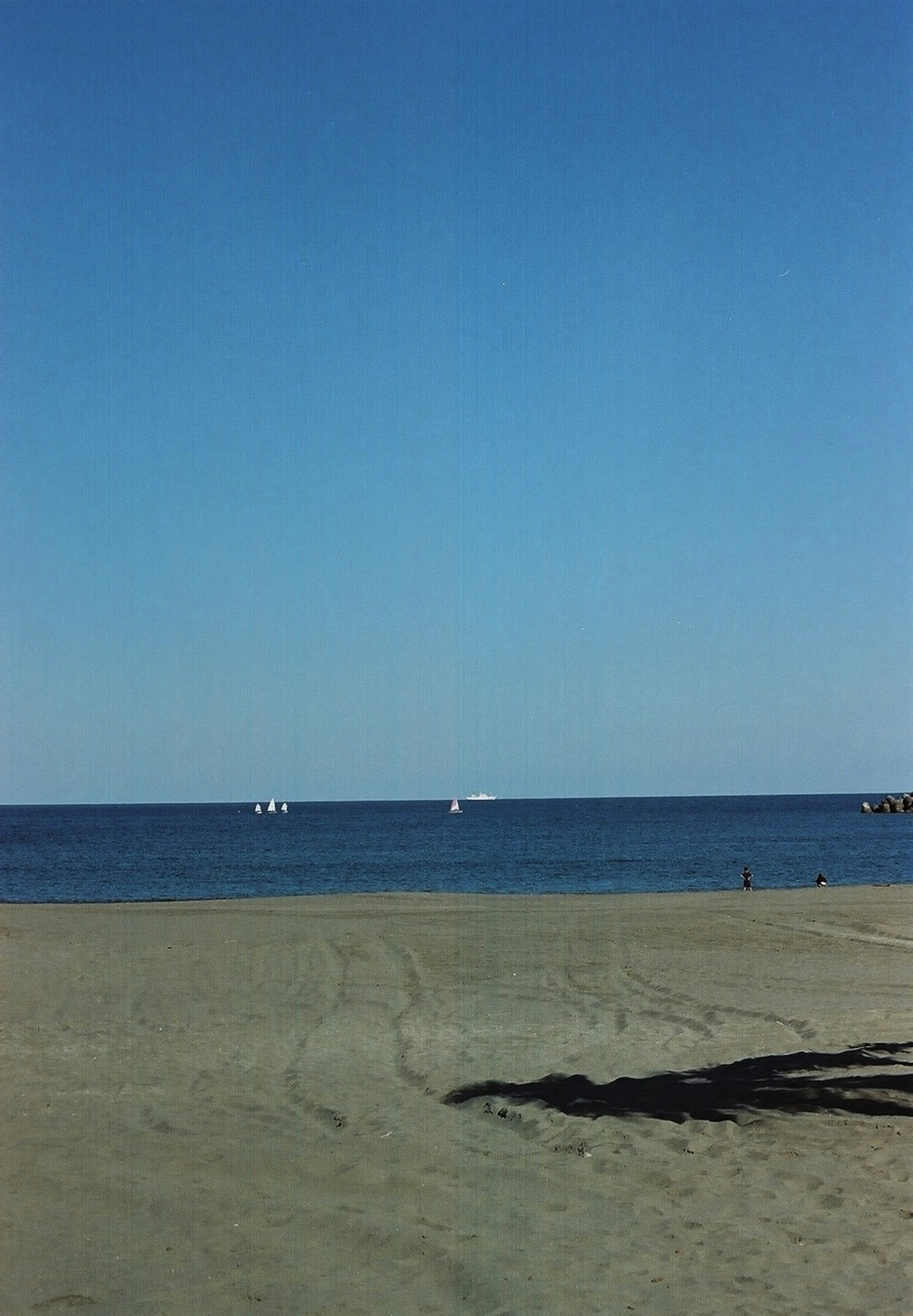 A clear blue sky over a calm sea with a sandy beach and a shadow