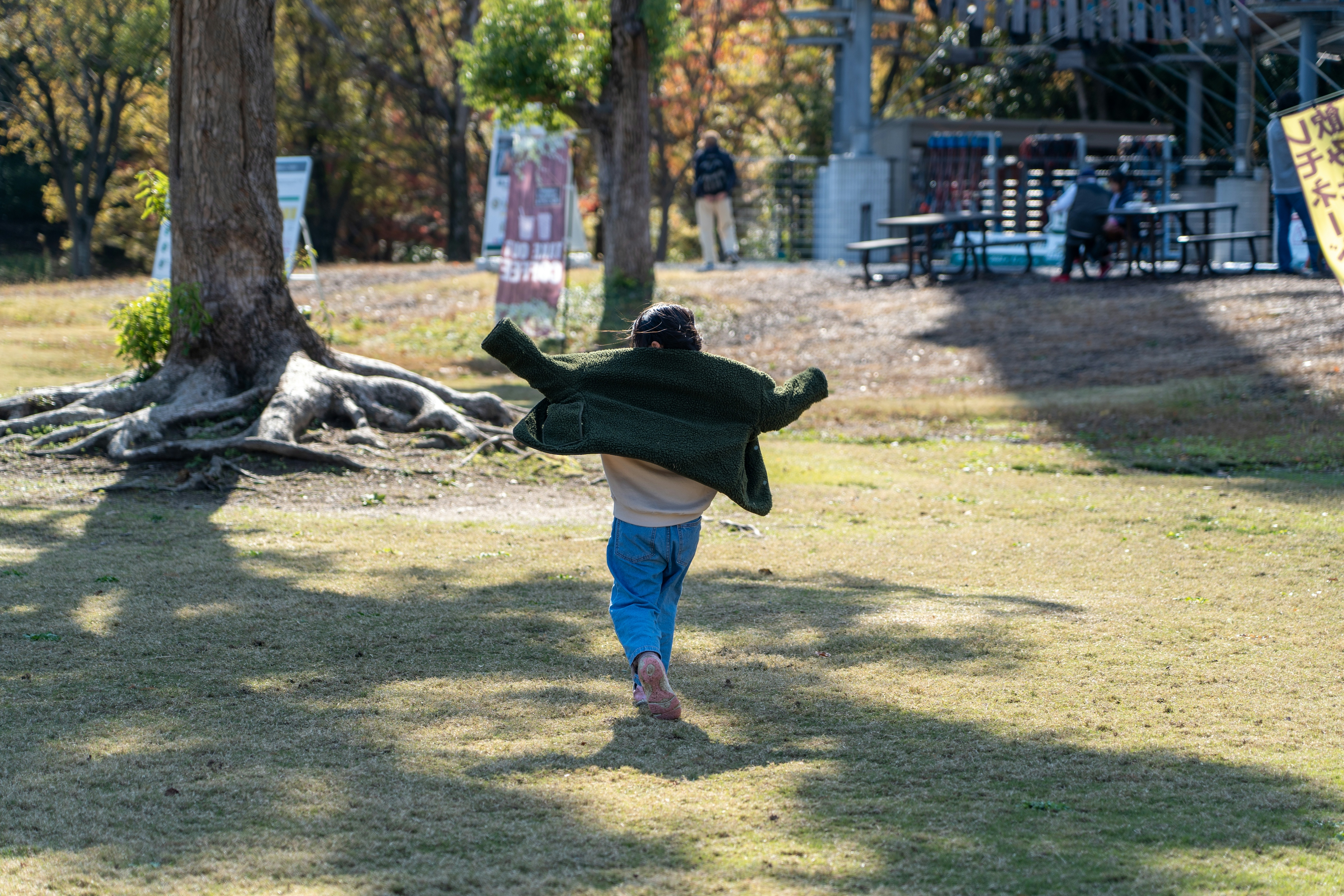 子供が公園で緑のコートを羽織りながら走っているシーン