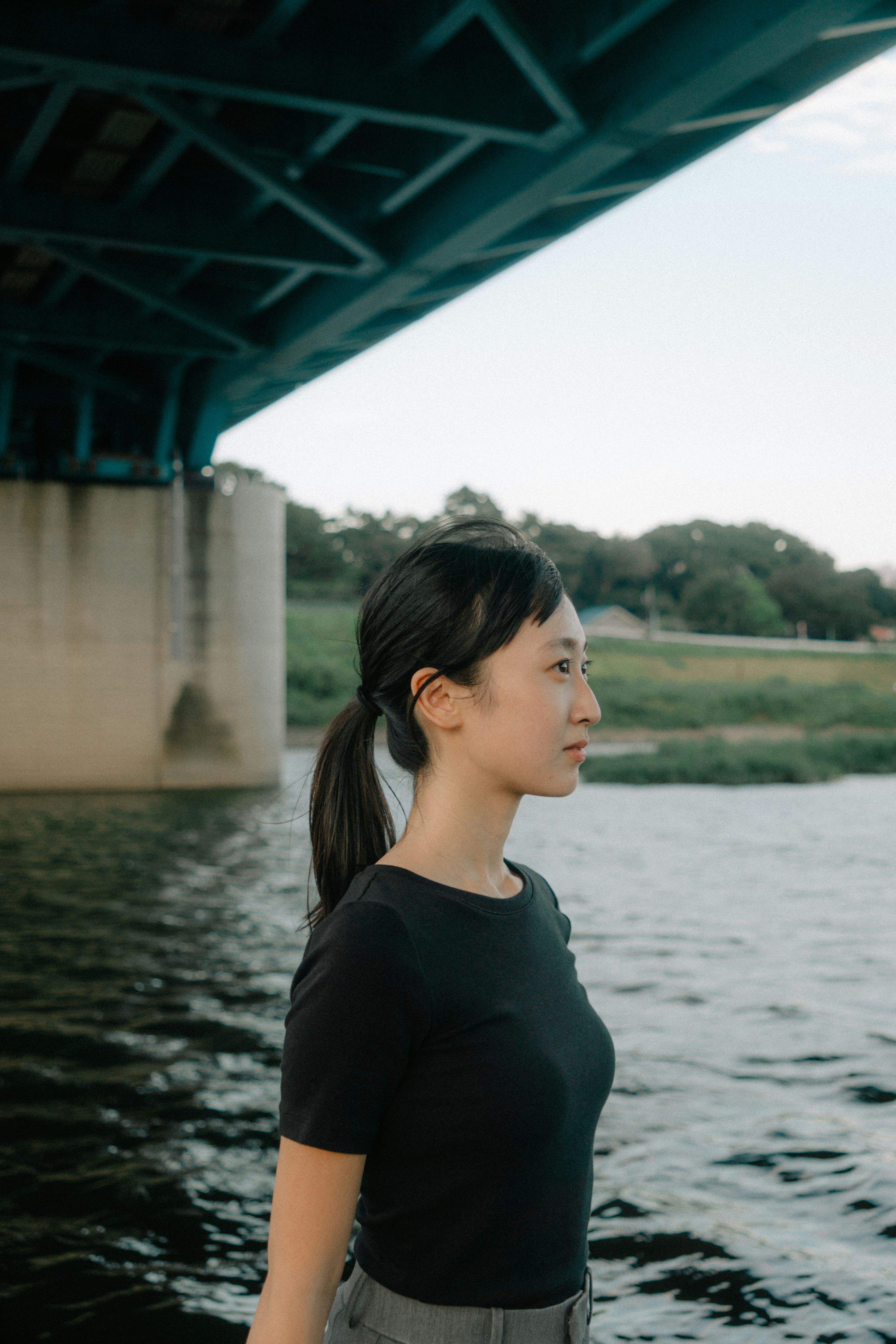 Profil d'une femme se tenant au bord de l'eau sous un pont bleu