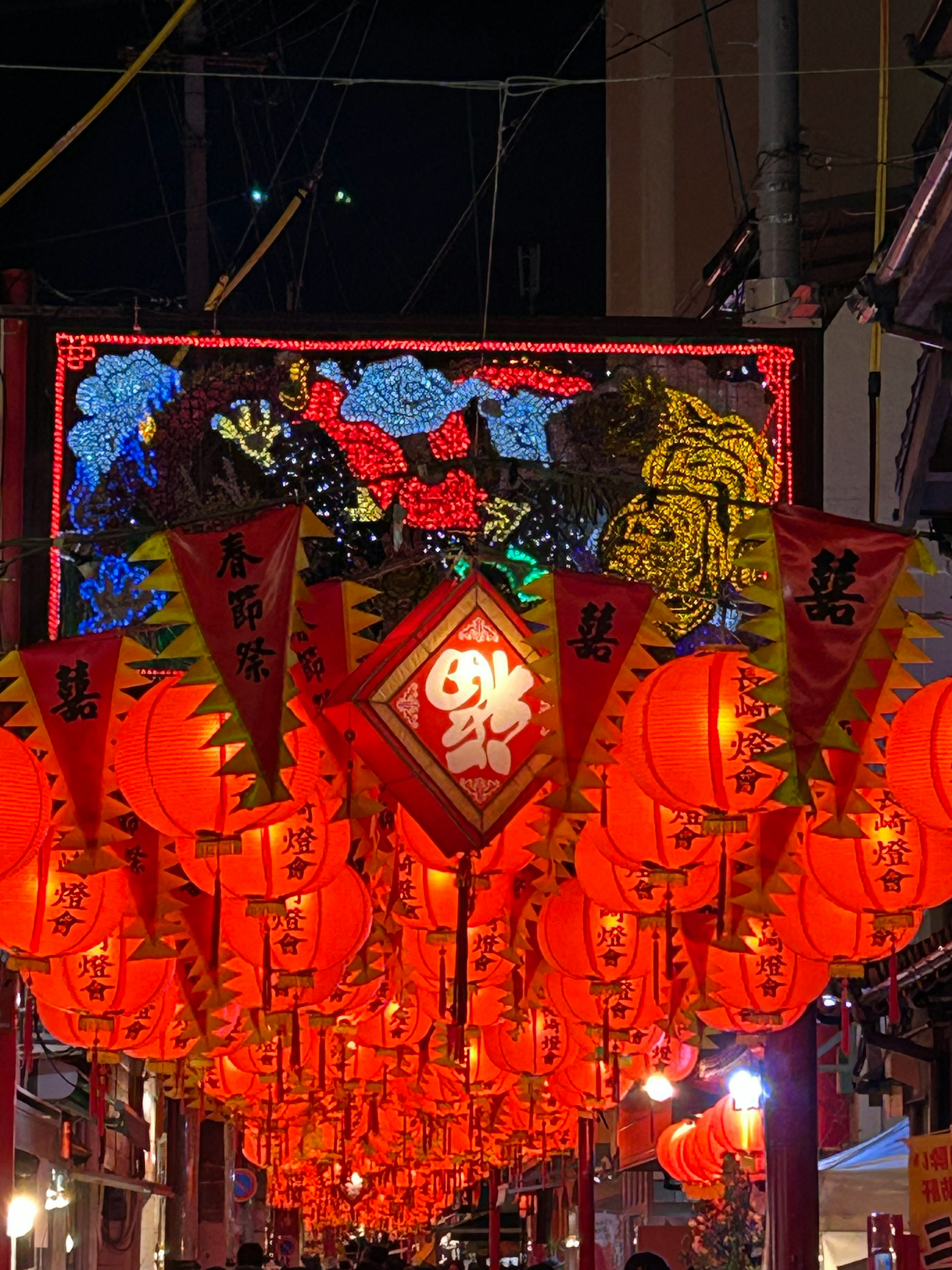 Rote Laternen hängen in einer nächtlichen Straße mit einem bunten Blumenschild