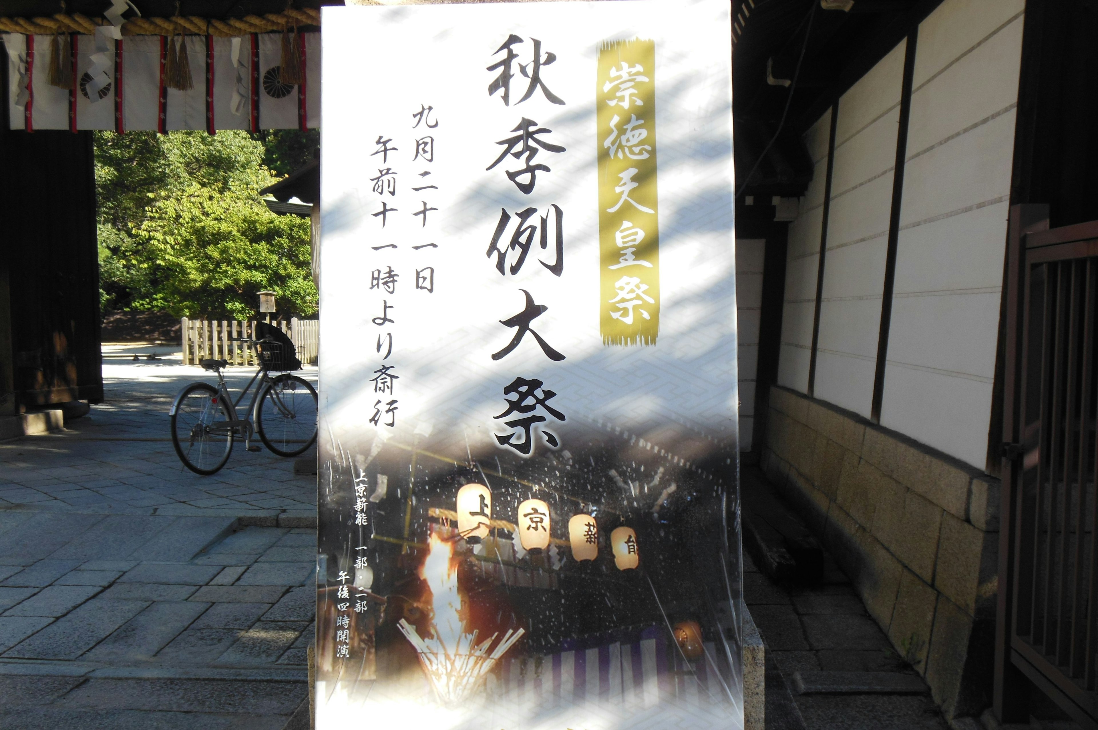 秋季节日的告示牌，背景有自行车和神社建筑