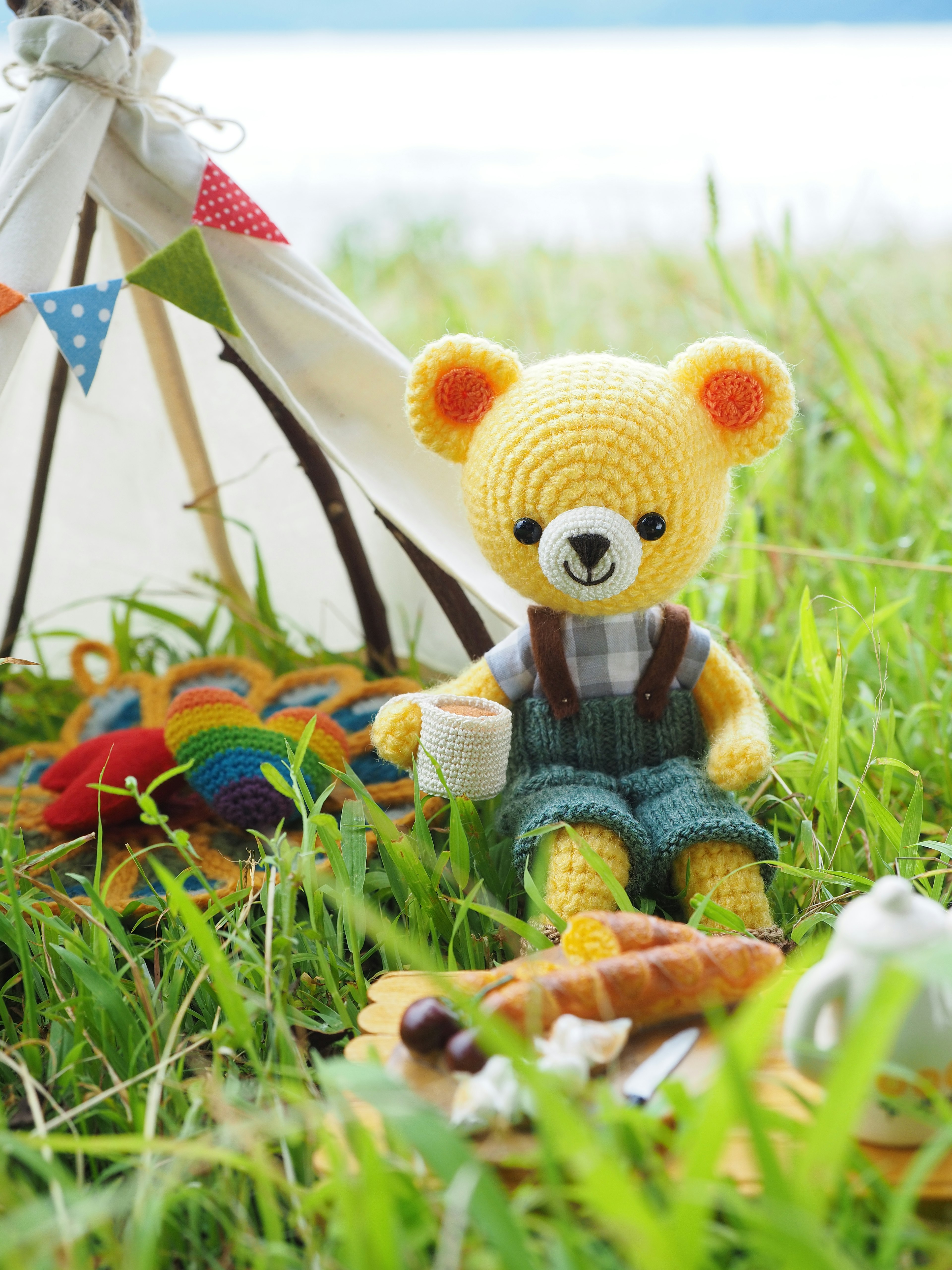 Un lindo oso de peluche amarillo sentado frente a una tienda en hierba verde con comida cerca