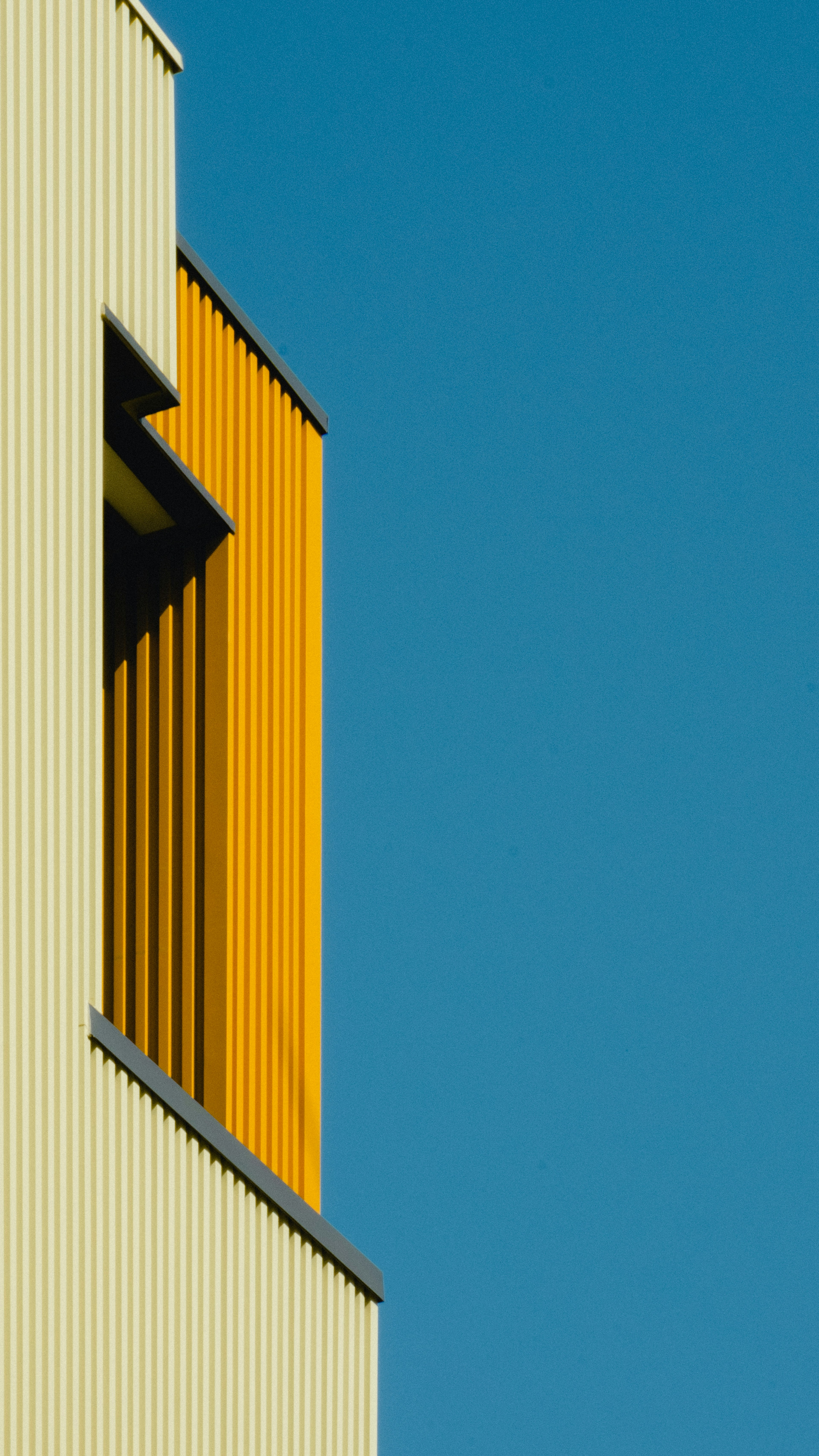 Moderne Gebäudeteil mit gelbem Paneel und vertikalen Streifen vor blauem Himmel