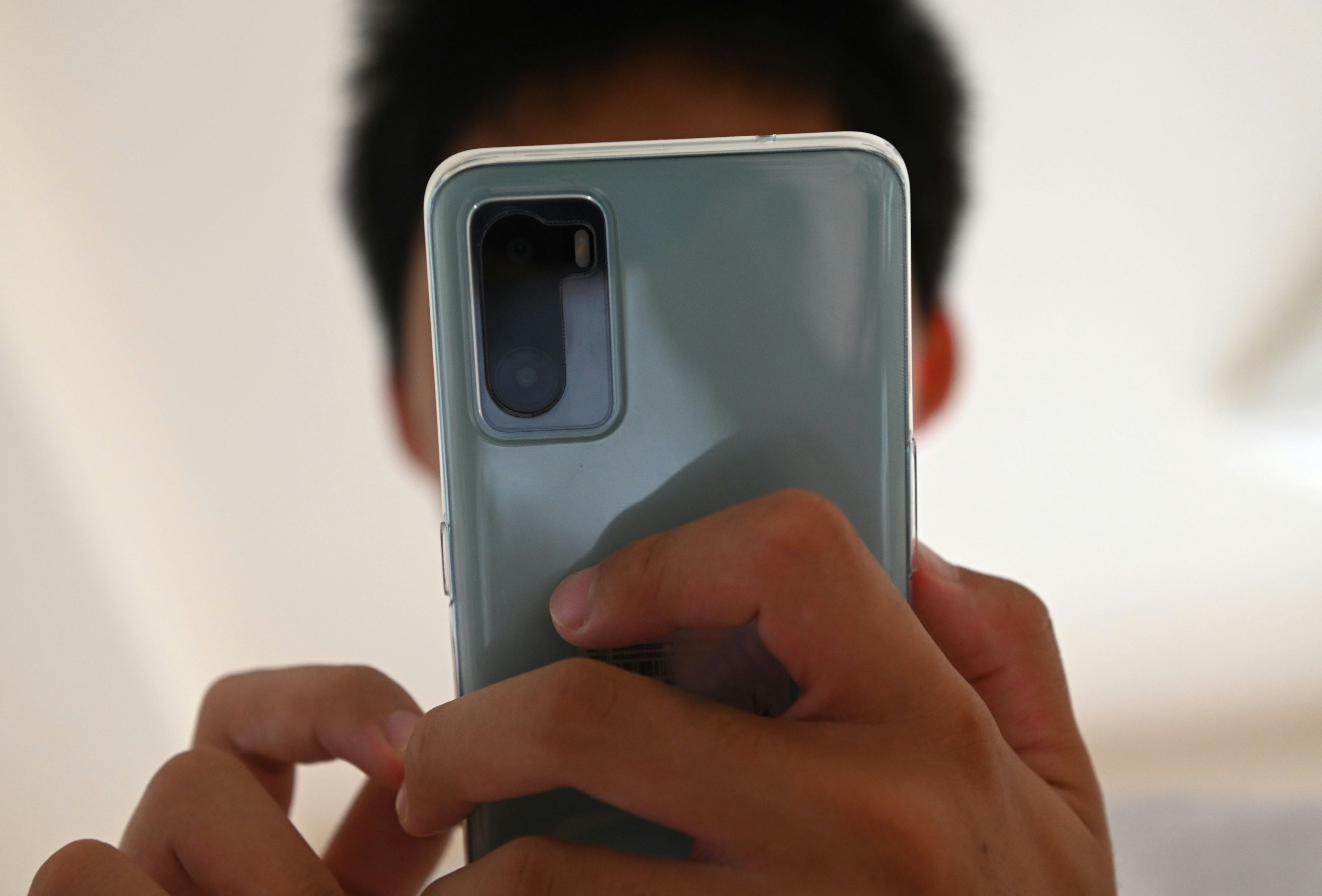 Gambar menunjukkan belakang smartphone yang dipegang di tangan seseorang Belakangnya berwarna biru muda dengan lensa kamera yang terlihat