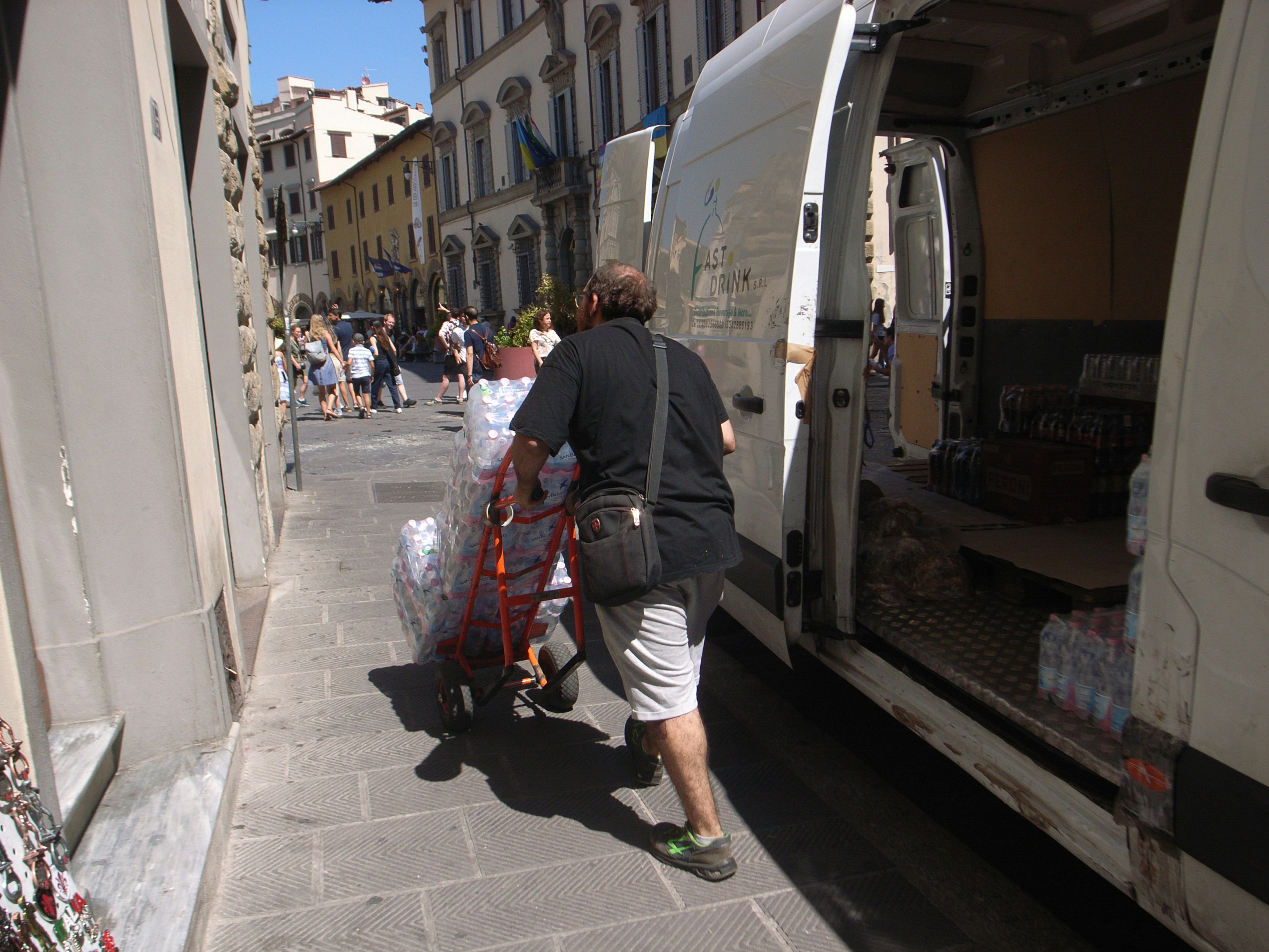 Una persona che spinge un carrello per trasportare merci in una scena di strada affollata