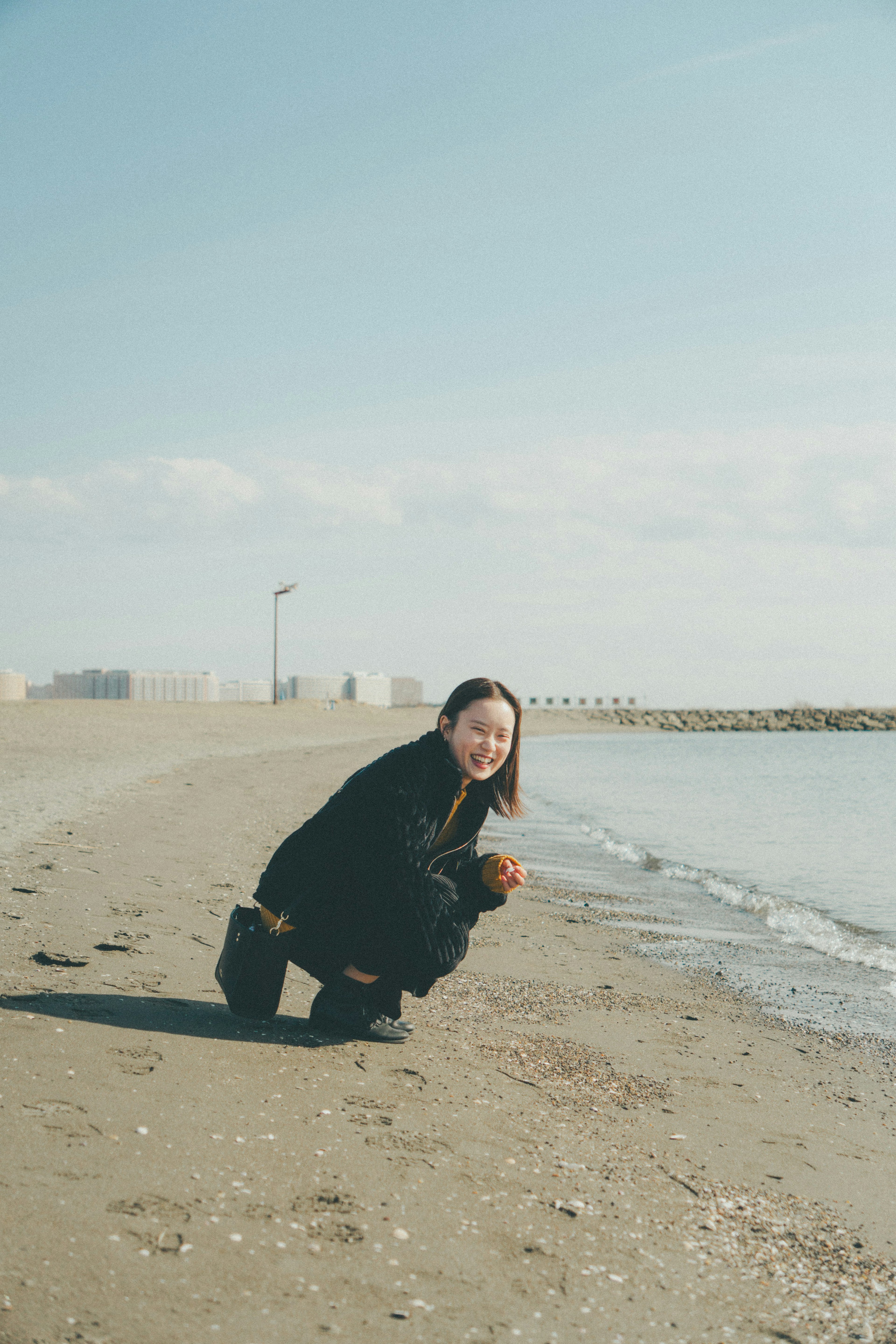 一位女性蹲在海边微笑穿着黑色衣服