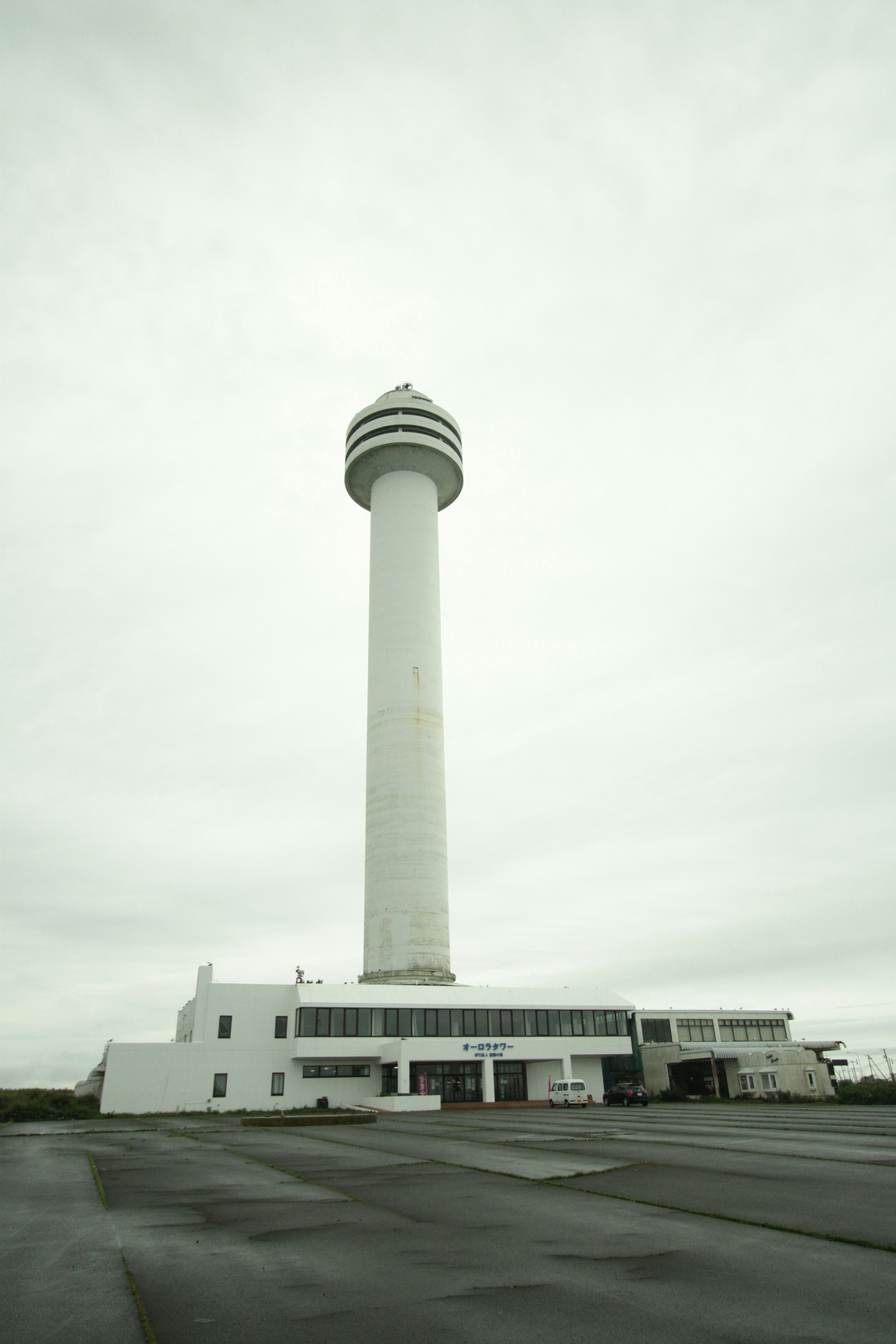 A tall white tower with a cylindrical top next to a low white building