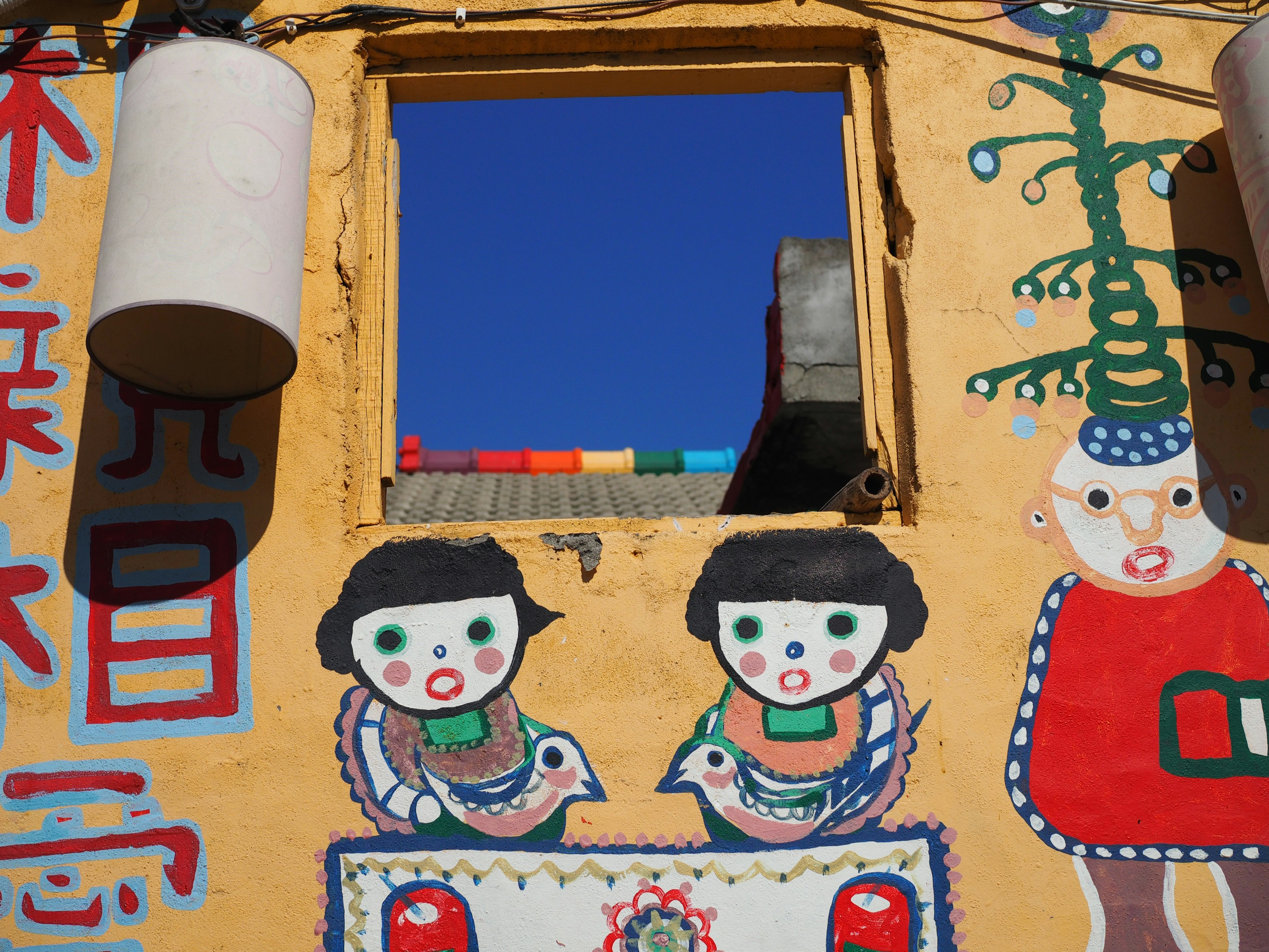 Buntes Wandgemälde mit Kindern und einem Fenster an einer gelben Wand