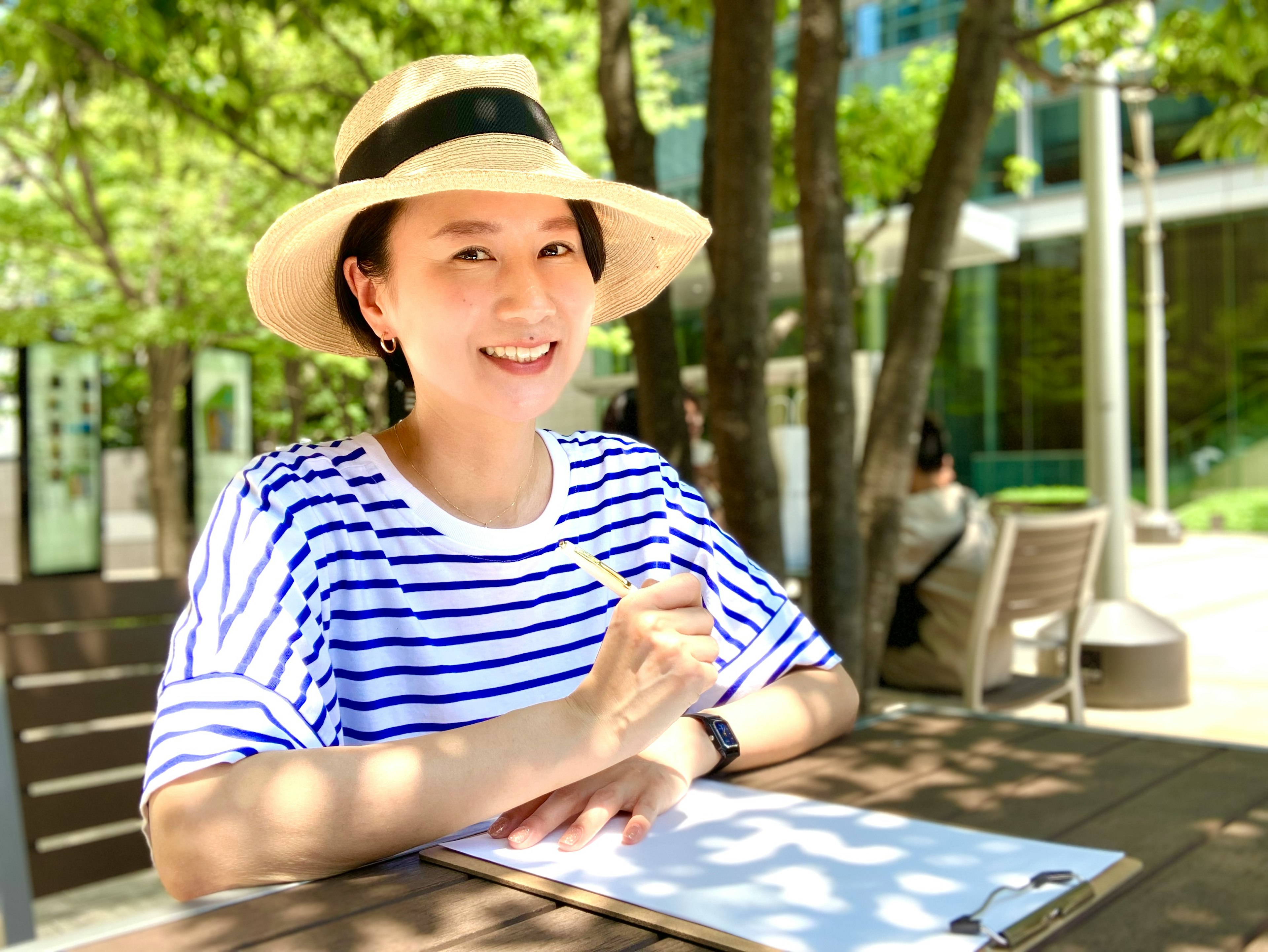 Une femme portant une chemise rayée et un chapeau en paille souriant à l'extérieur