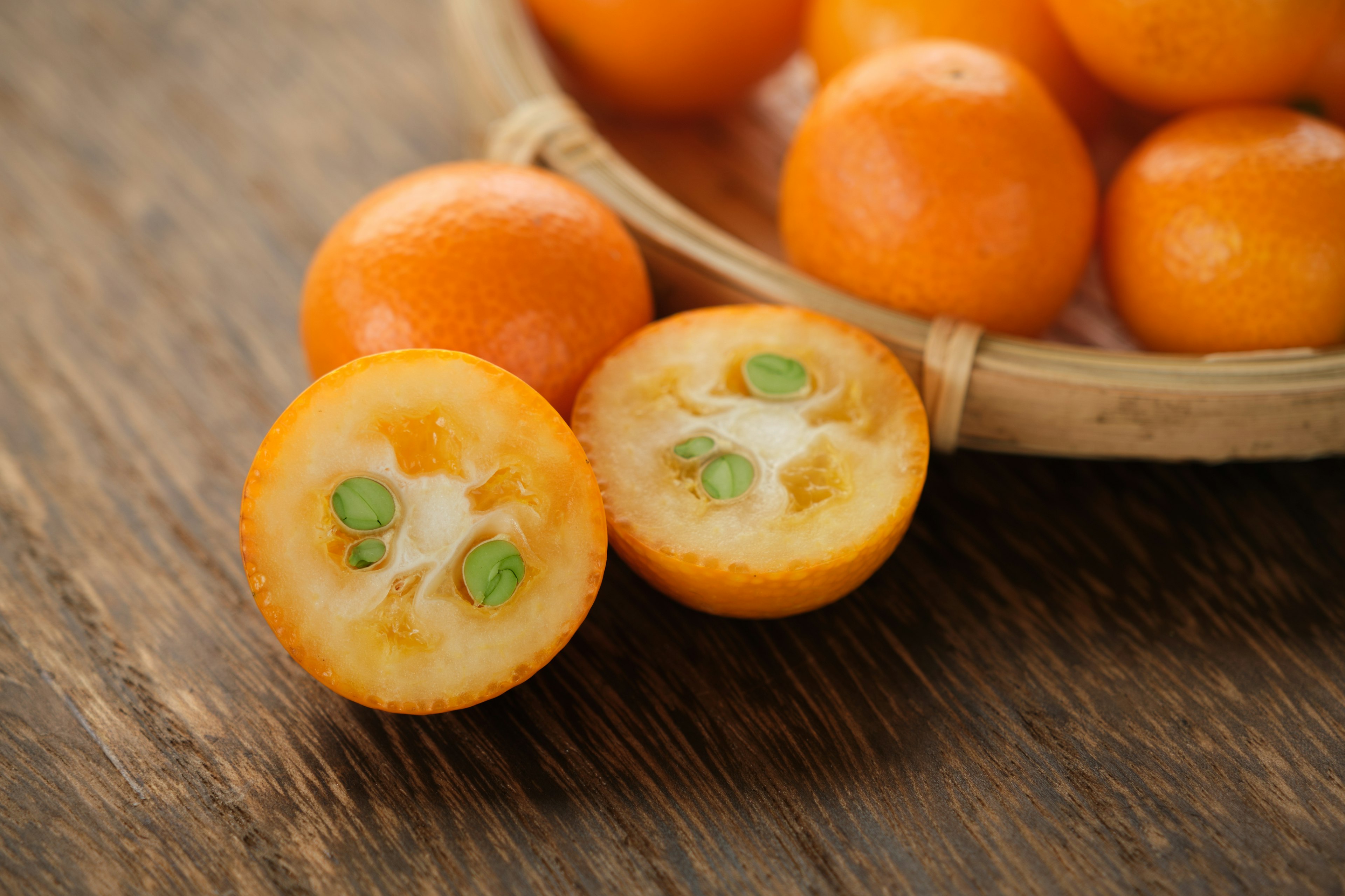 Image of orange fruits in a basket with a halved fruit showing seeds