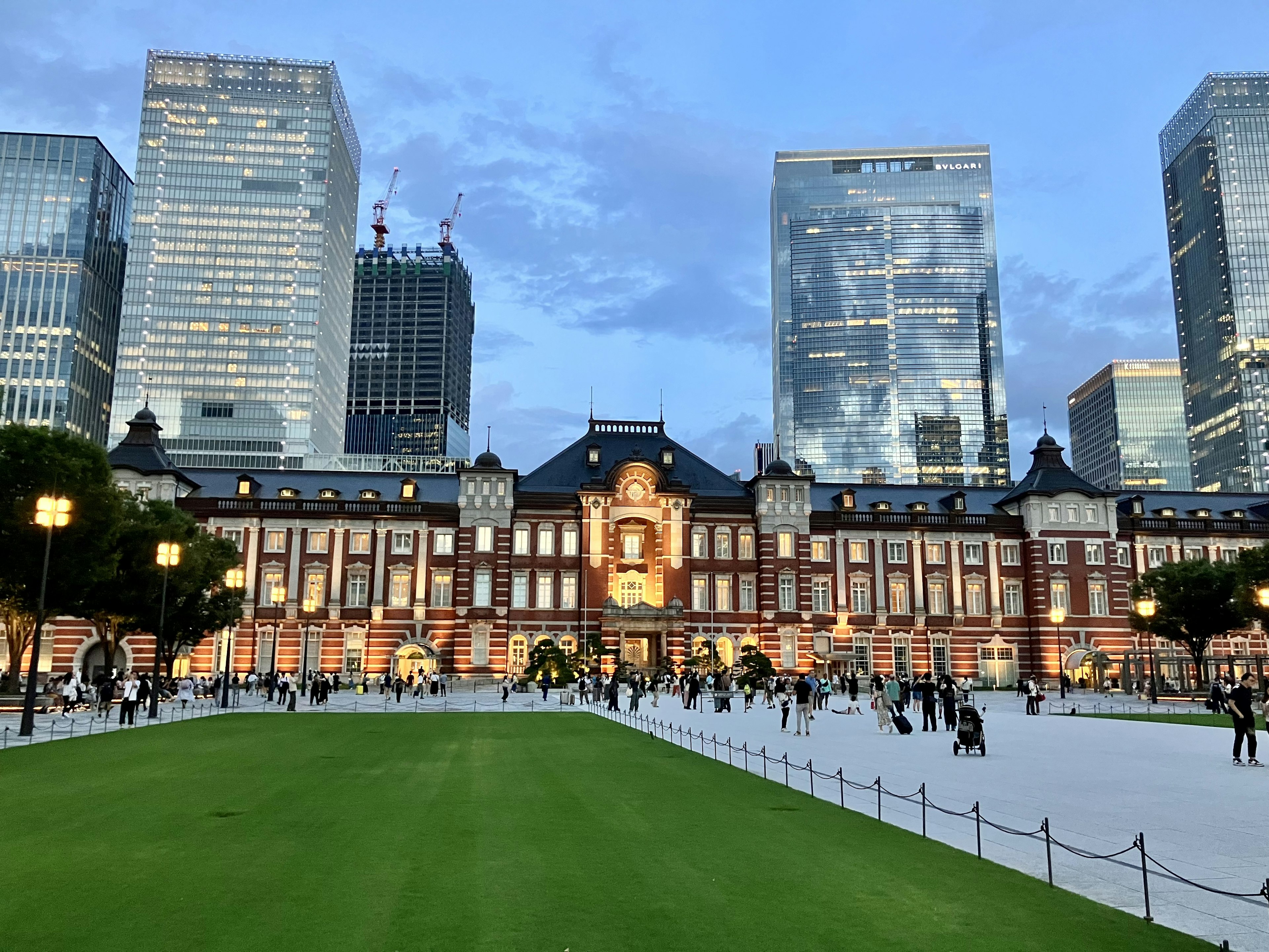 東京駅の歴史的な建物と近代的な高層ビルのコントラスト広い緑地に人々が歩いている