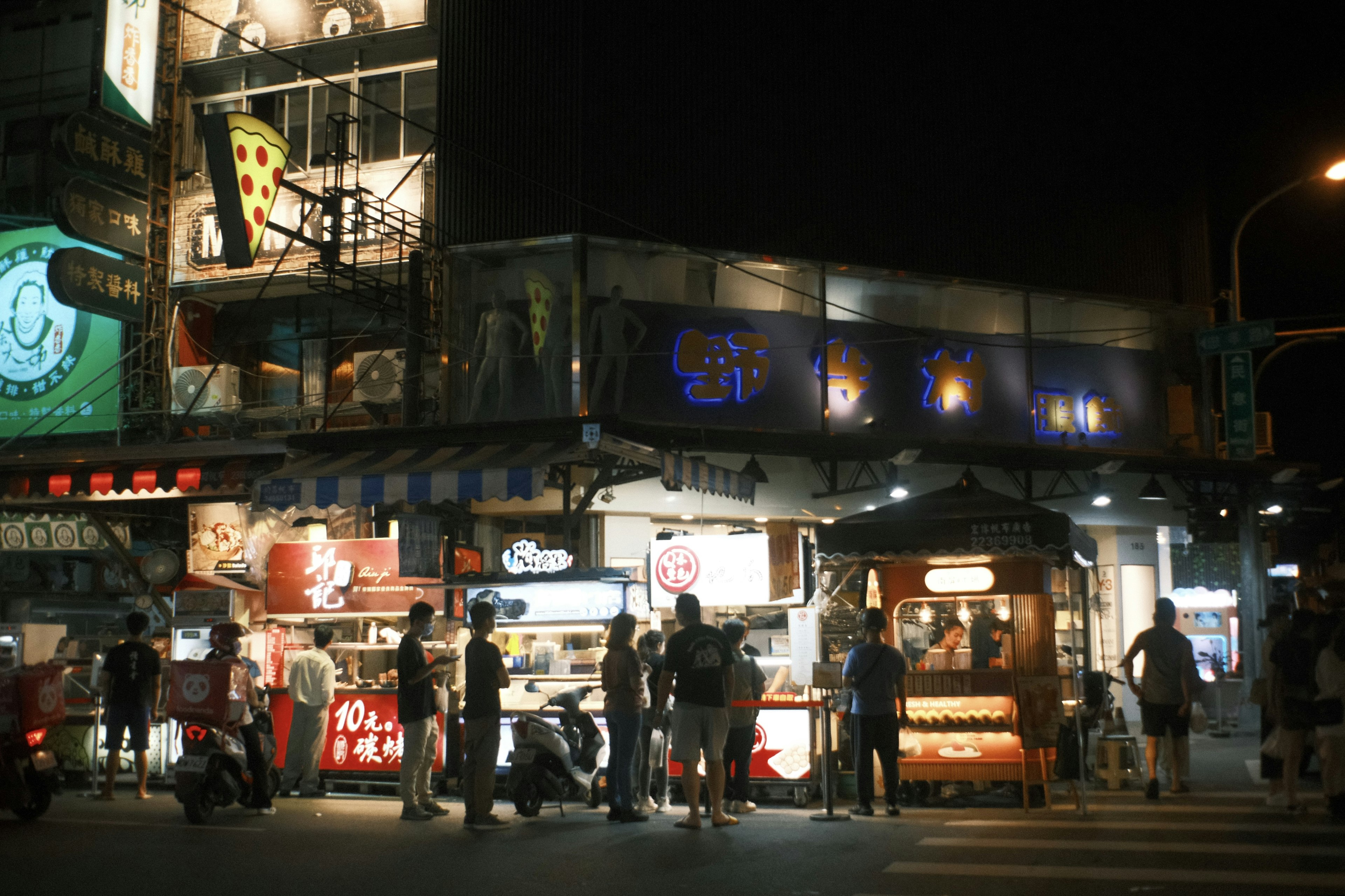 夜の屋台街の賑わいと明るい看板が特徴的な風景