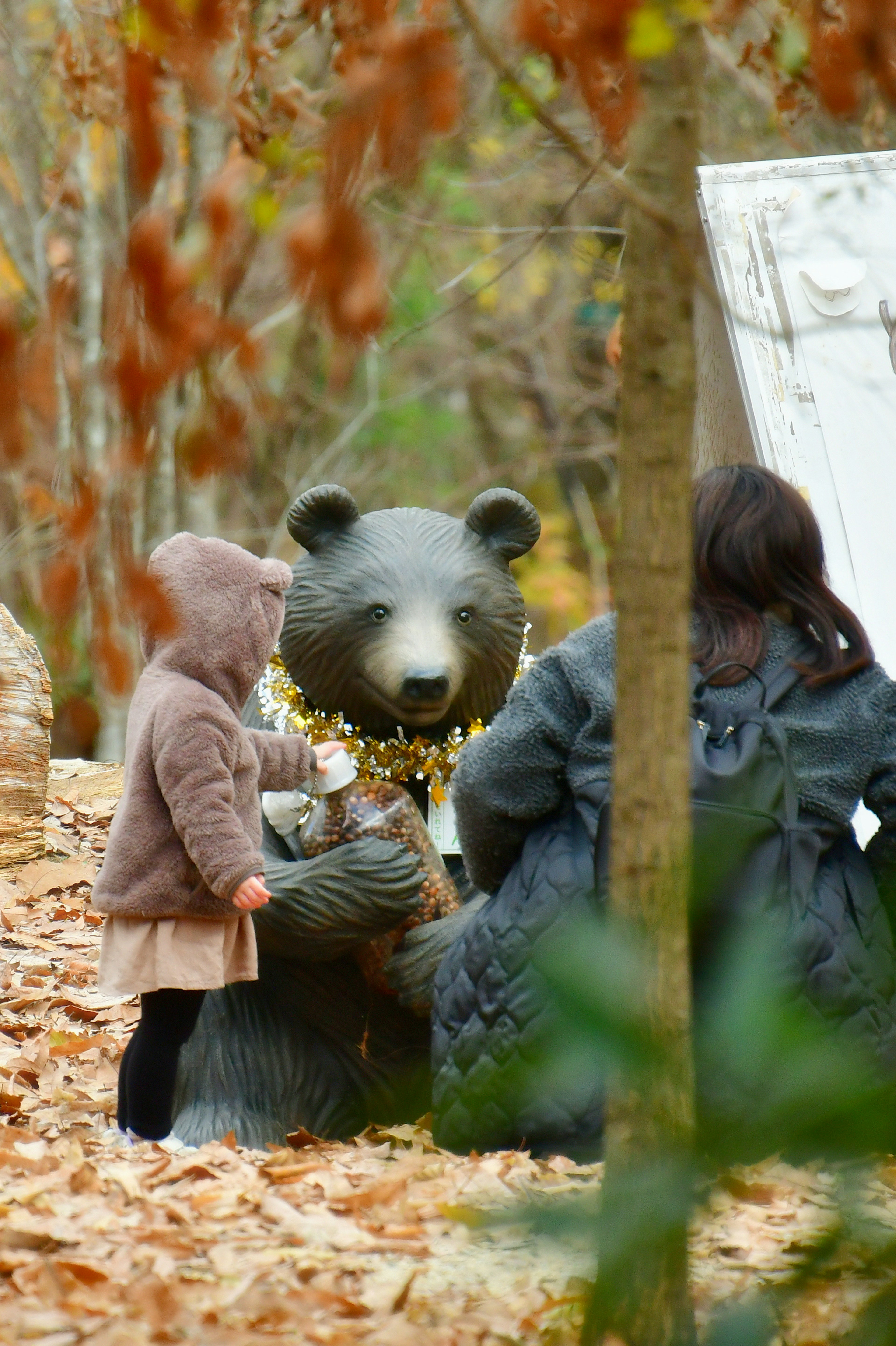 A child playing with a bear statue in a forest setting