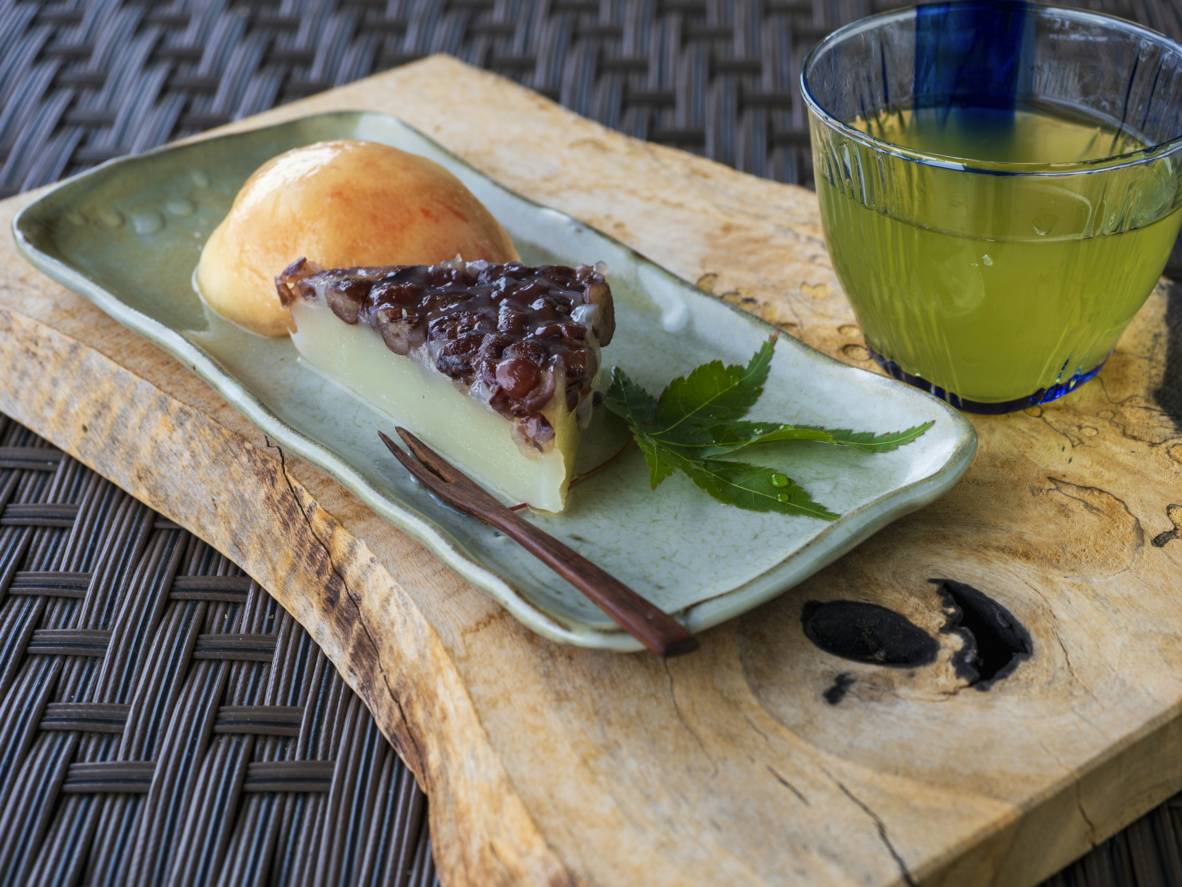 Ein grüner Teller mit einem Stück japanischer Süßigkeit, einem Brötchen und einem Getränk