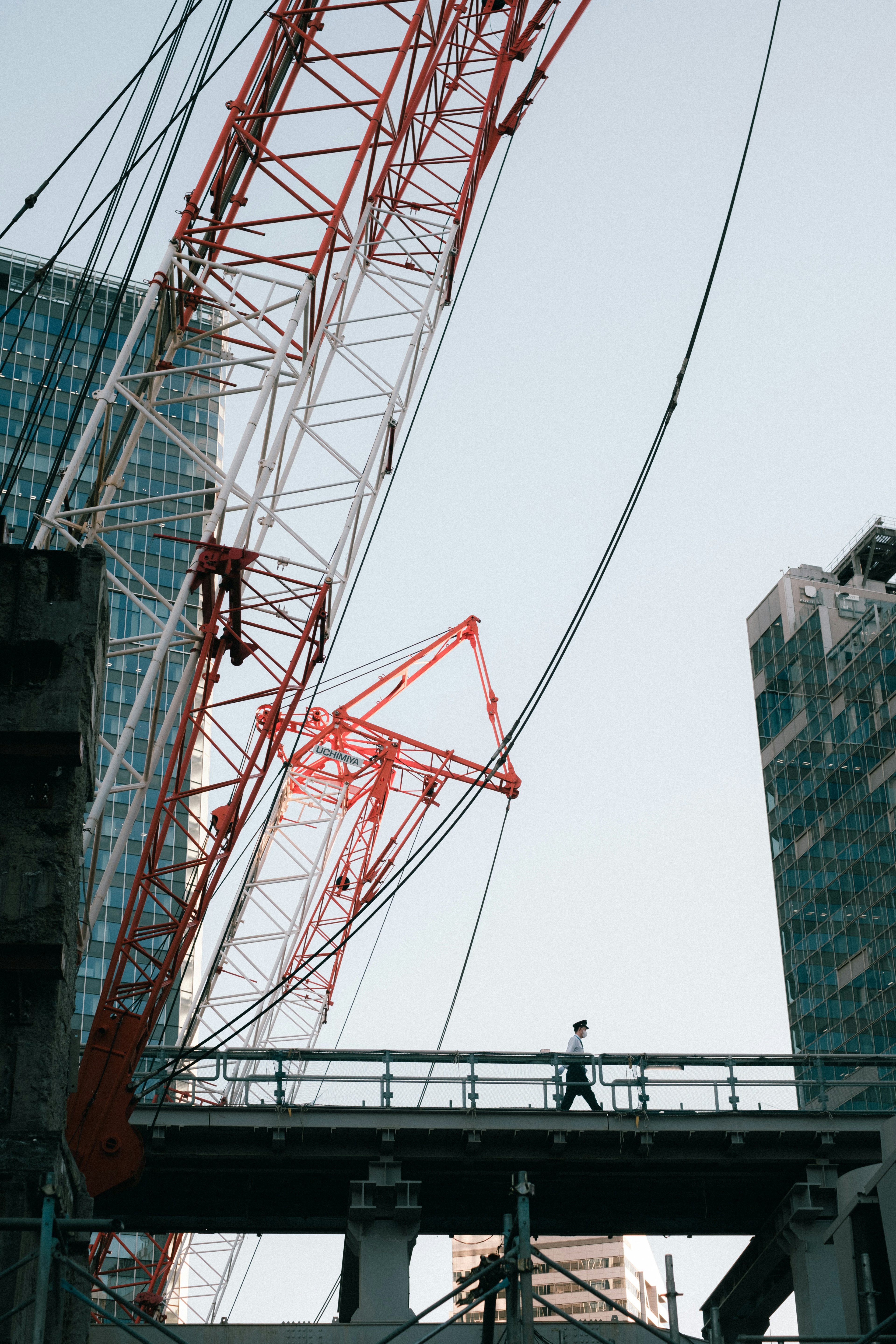 Person walking on bridge with red crane and skyscrapers in background