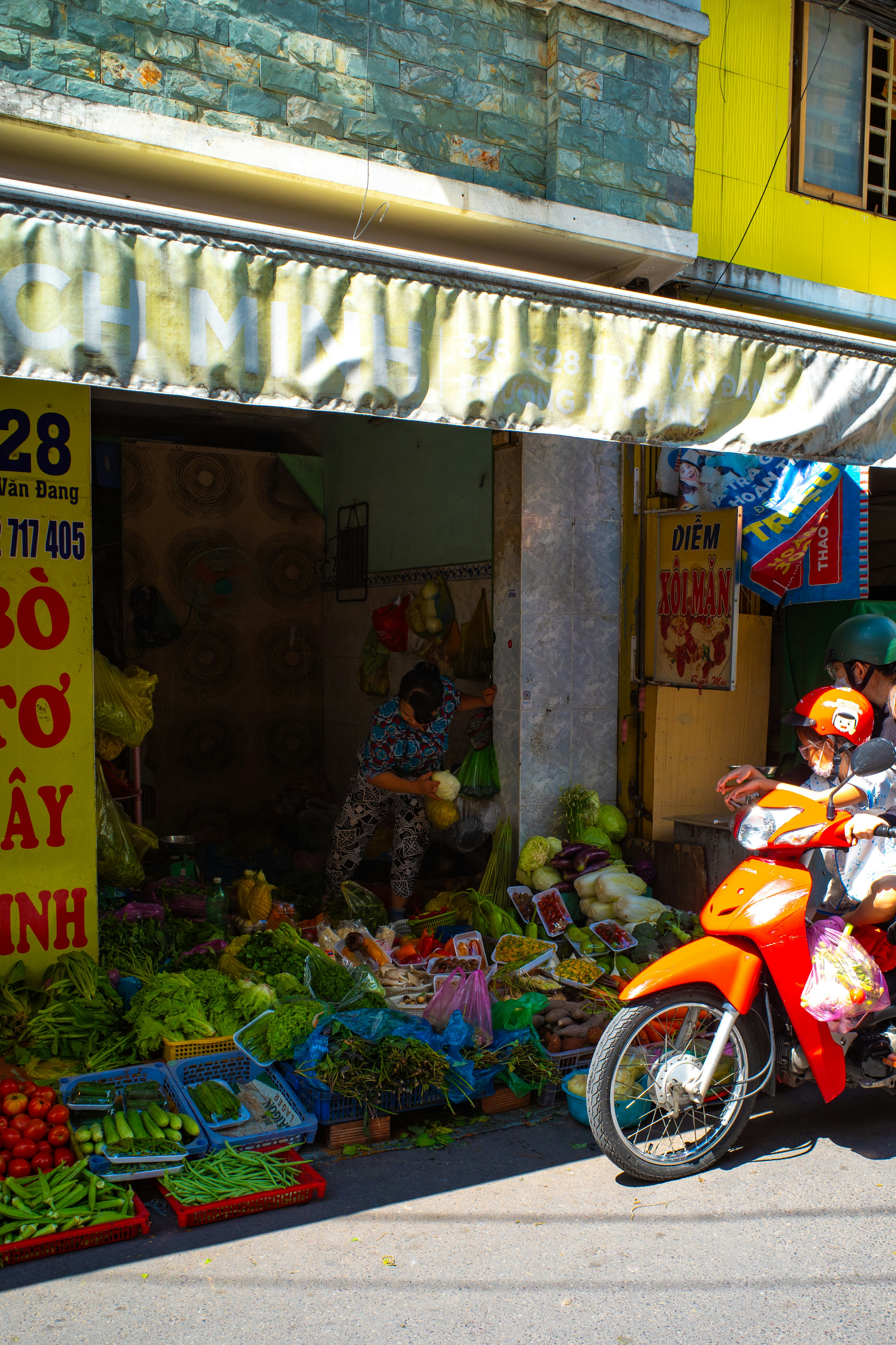 Exhibición vibrante de frutas y verduras frente a una tienda con una motocicleta pasando