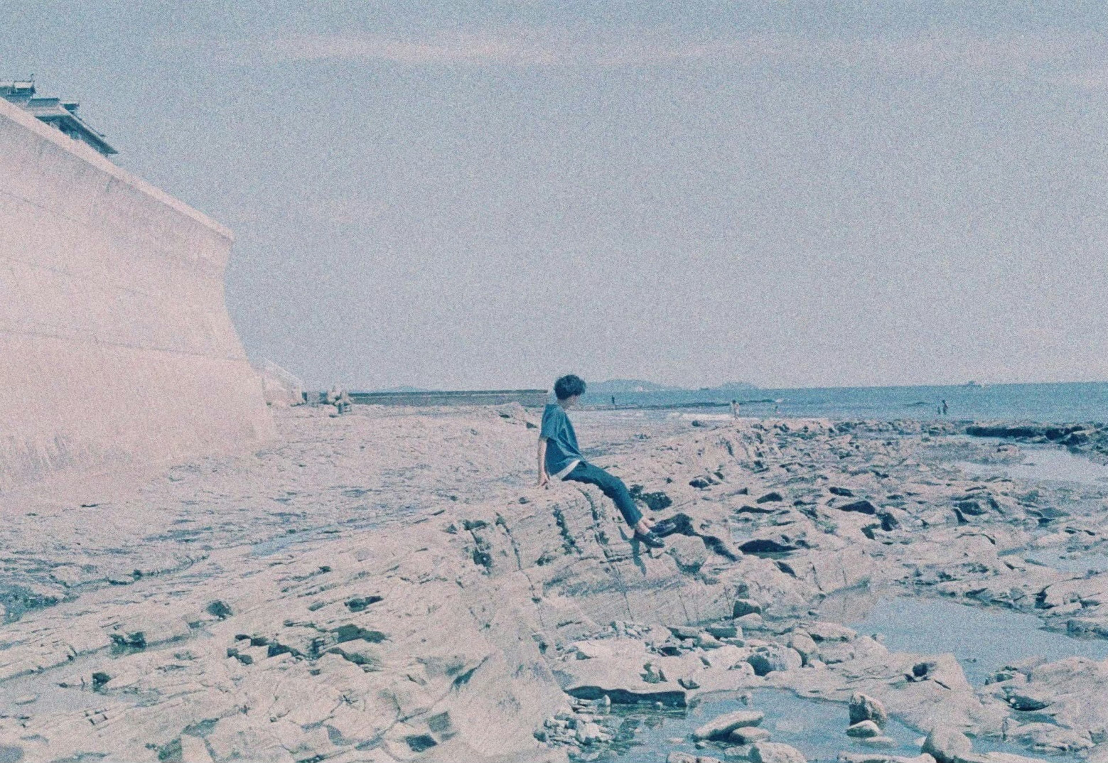 Person sitting on rocky shoreline with ocean view