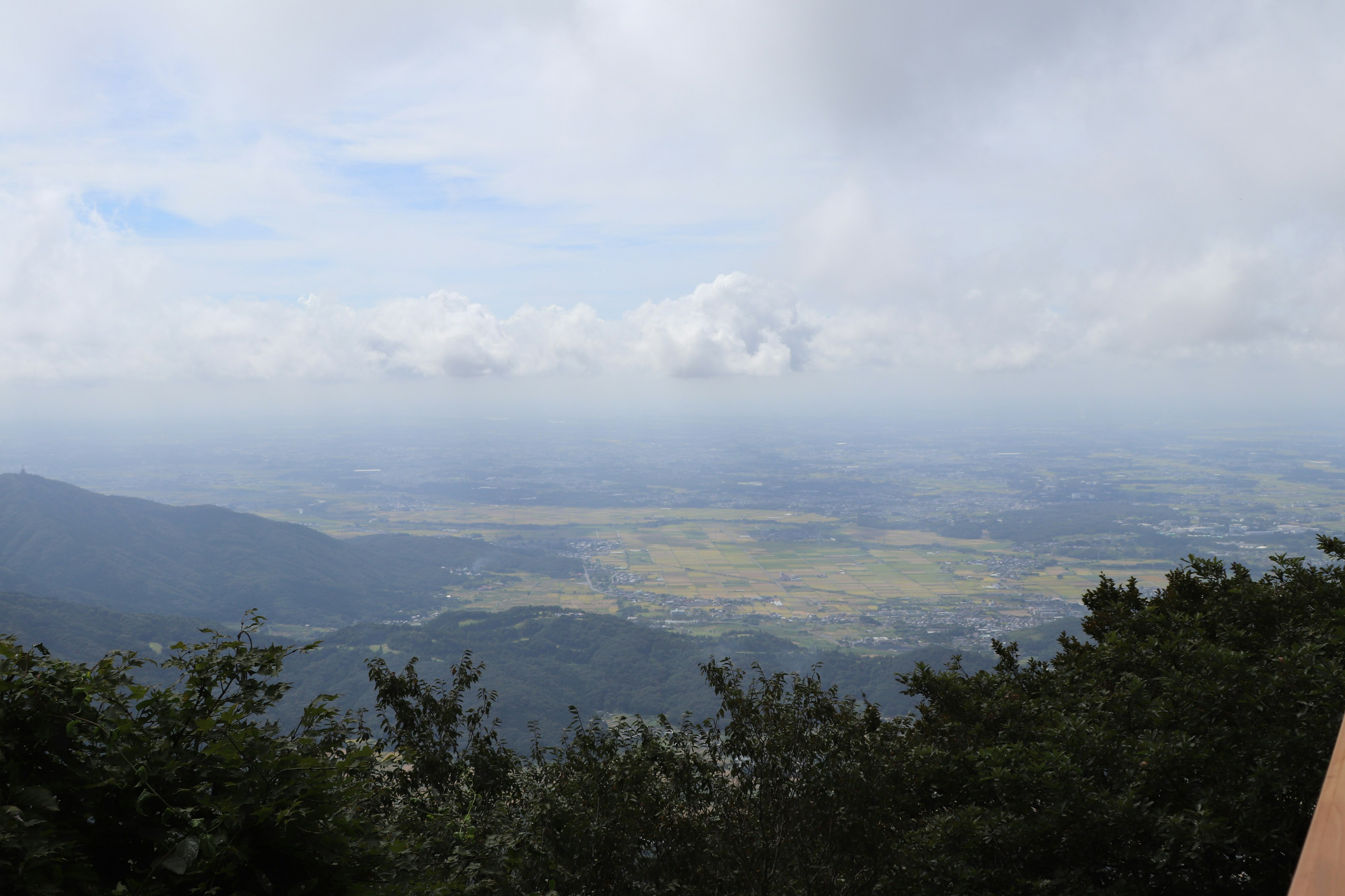 Expansive view from a mountain top with greenery and clouds in the background