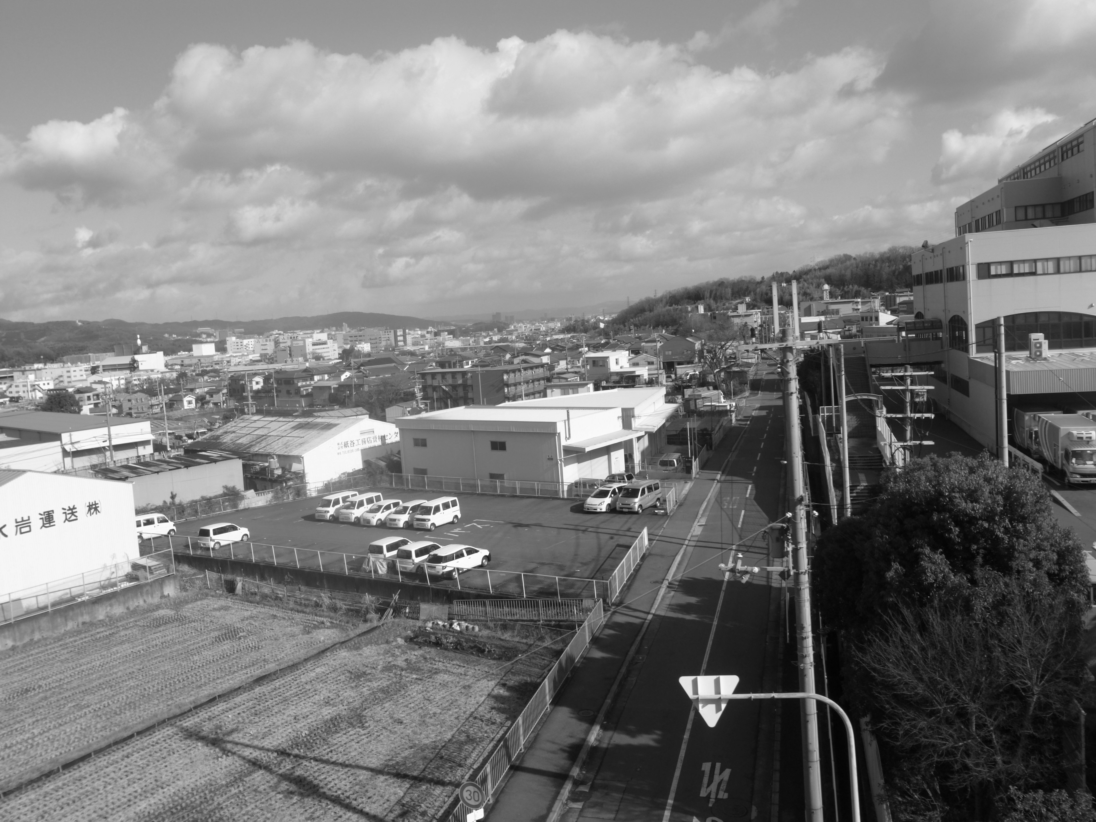 Paesaggio urbano in bianco e nero con fabbriche e veicoli, montagne visibili in lontananza