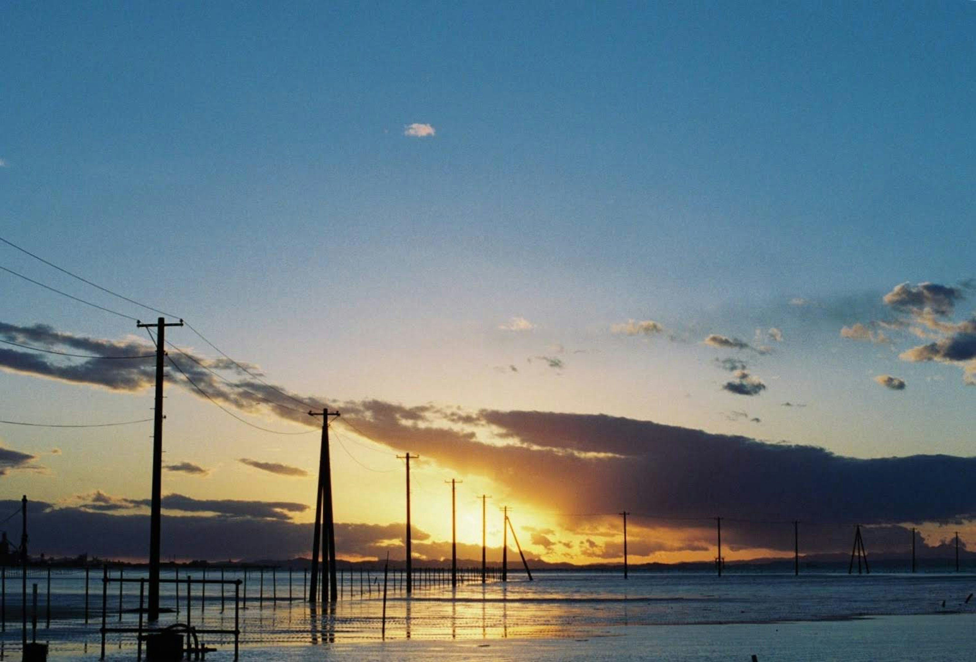 美しい夕焼けの空と水面に映る電信柱のシルエット