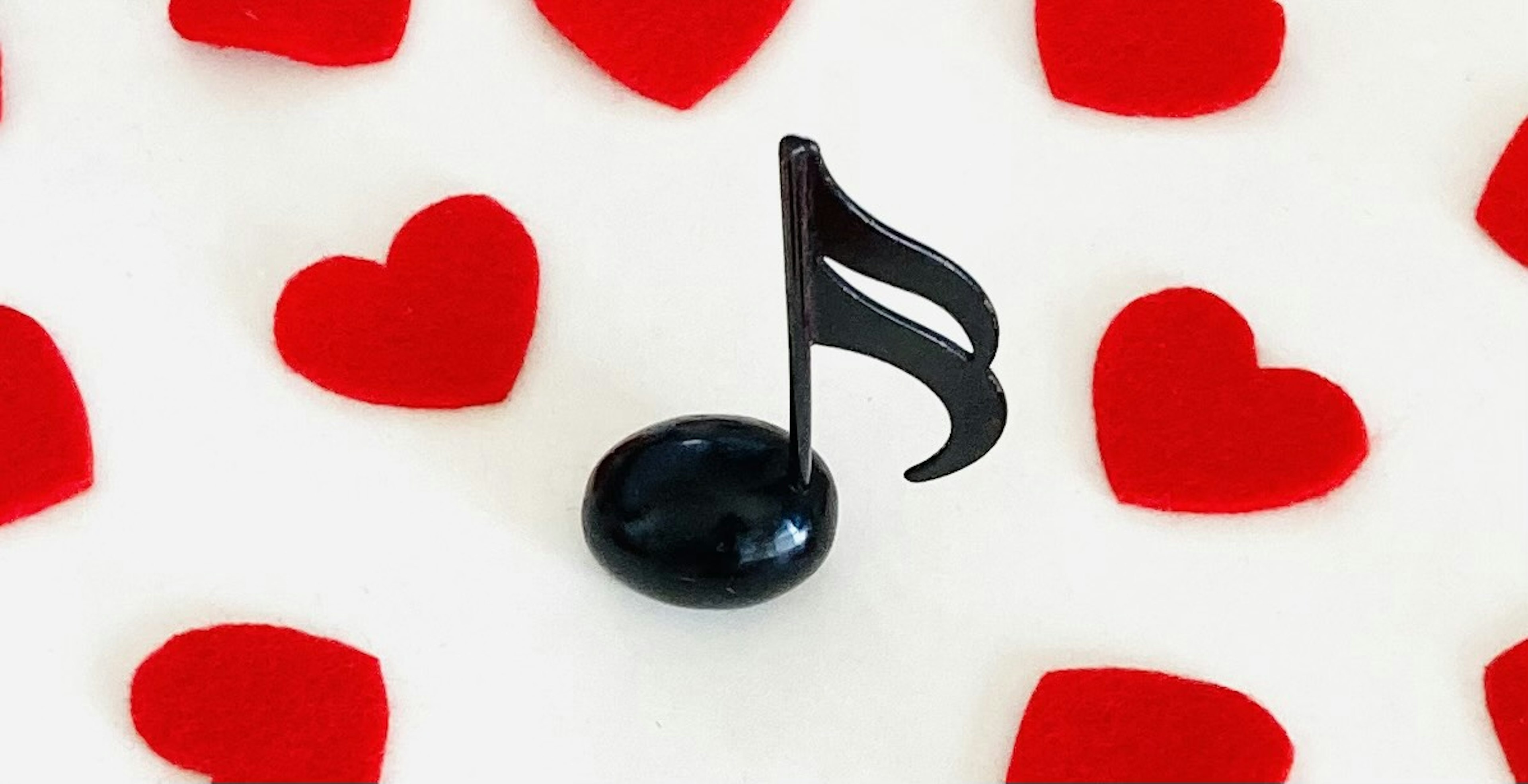 A black musical note on a white surface surrounded by red hearts