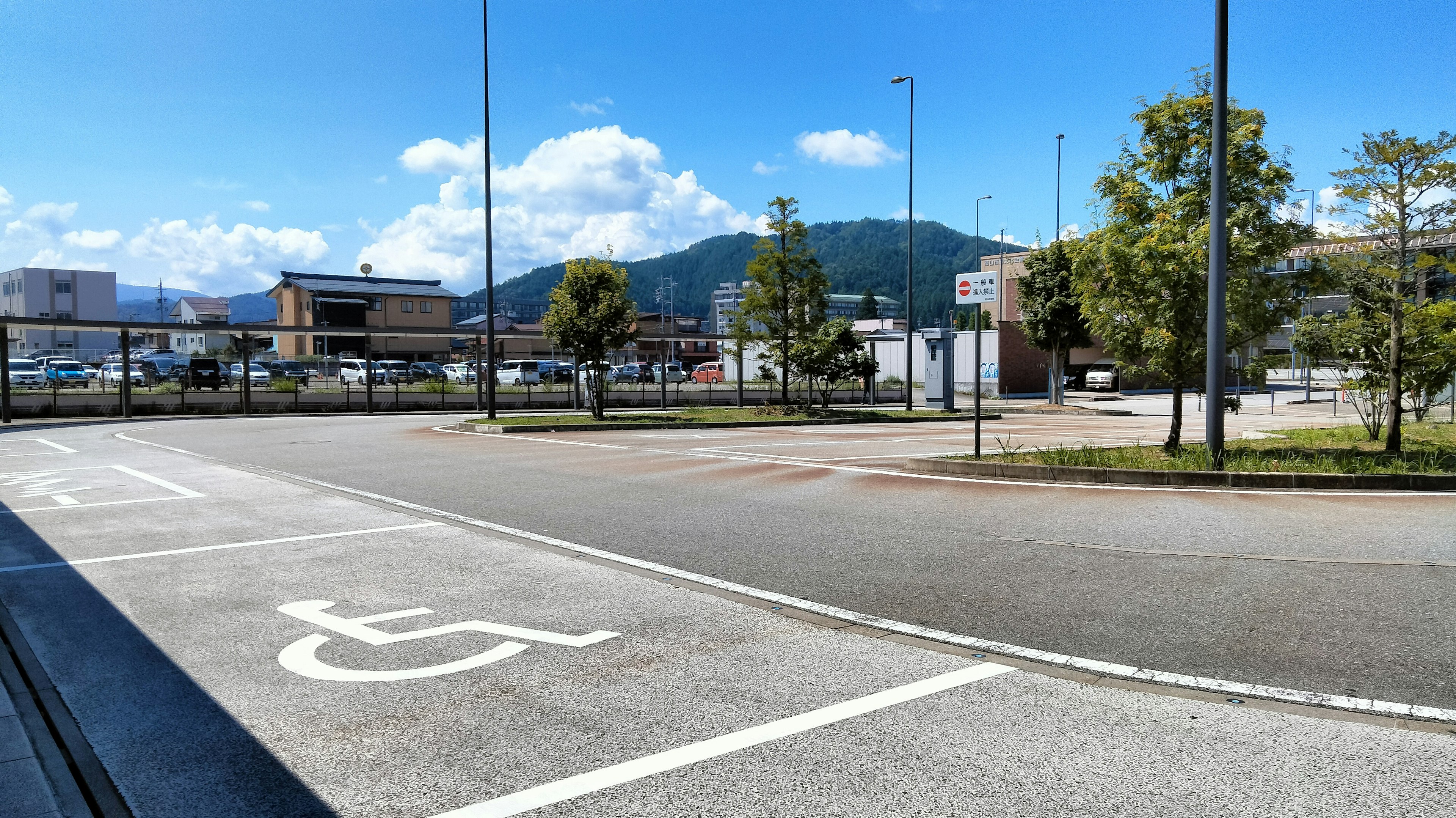 Spacious parking lot under blue sky featuring accessible parking space and surrounding trees