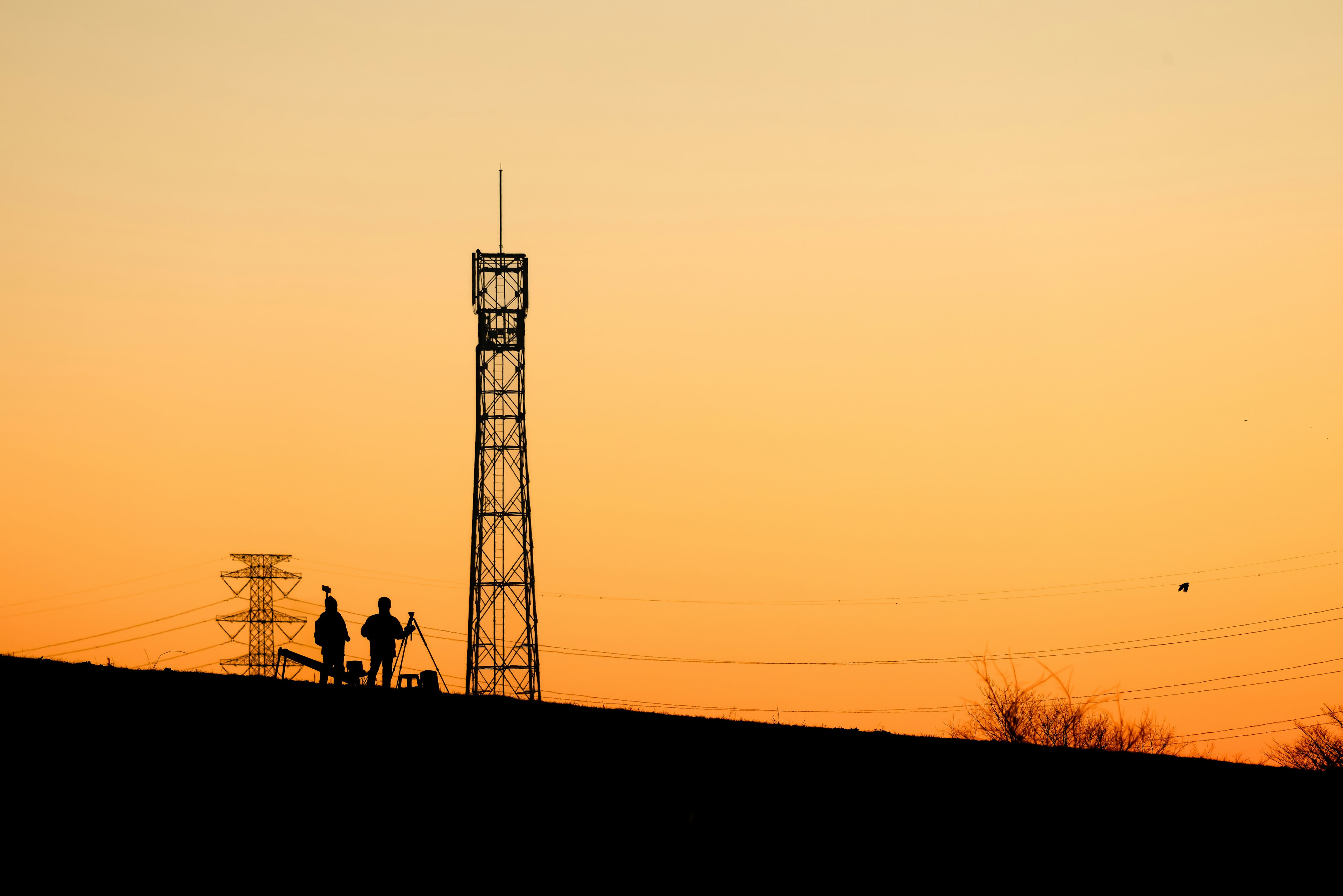 Figuras en silueta contra un atardecer con una torre de comunicación