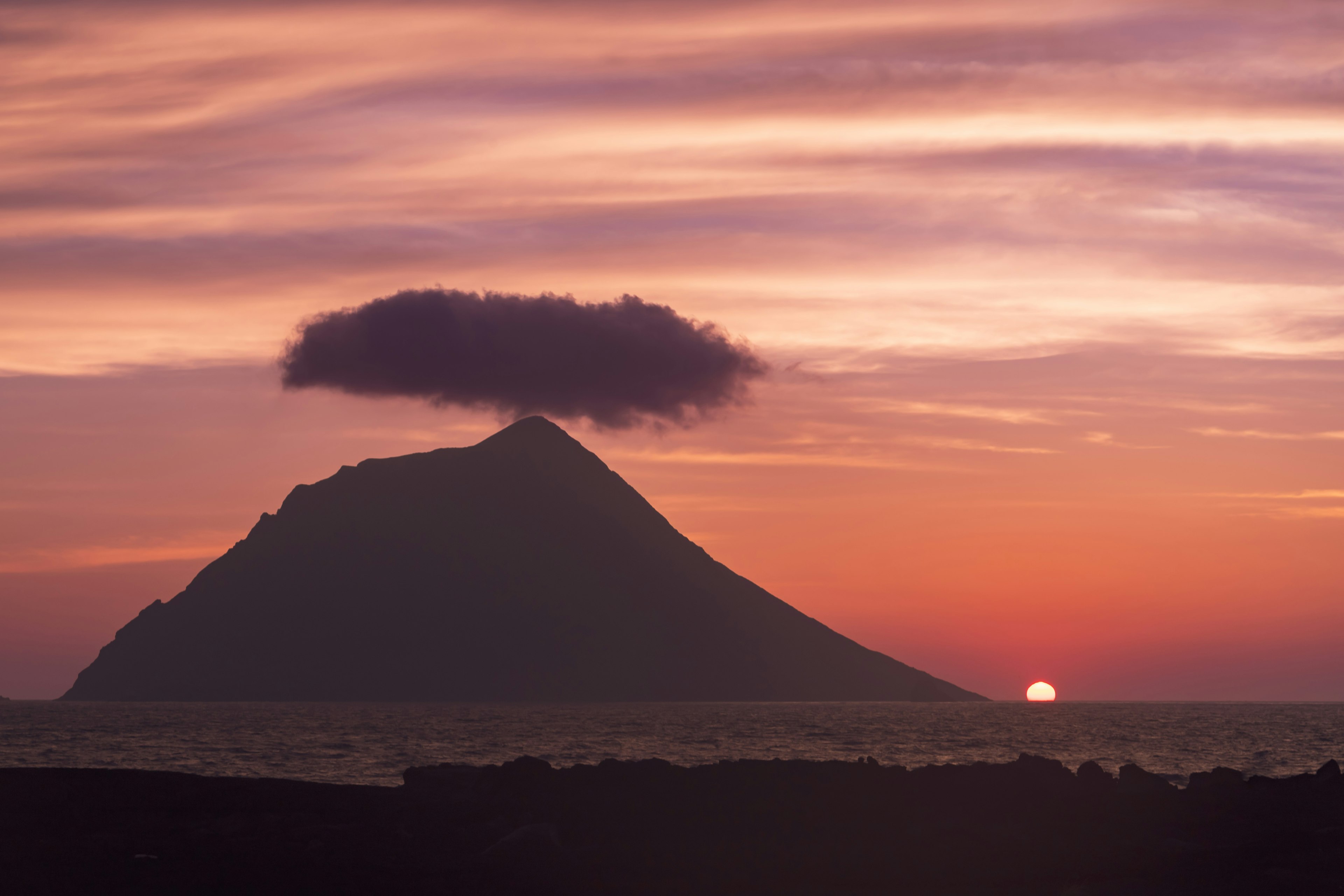 Silhouette of a mountain with a cloud at sunset