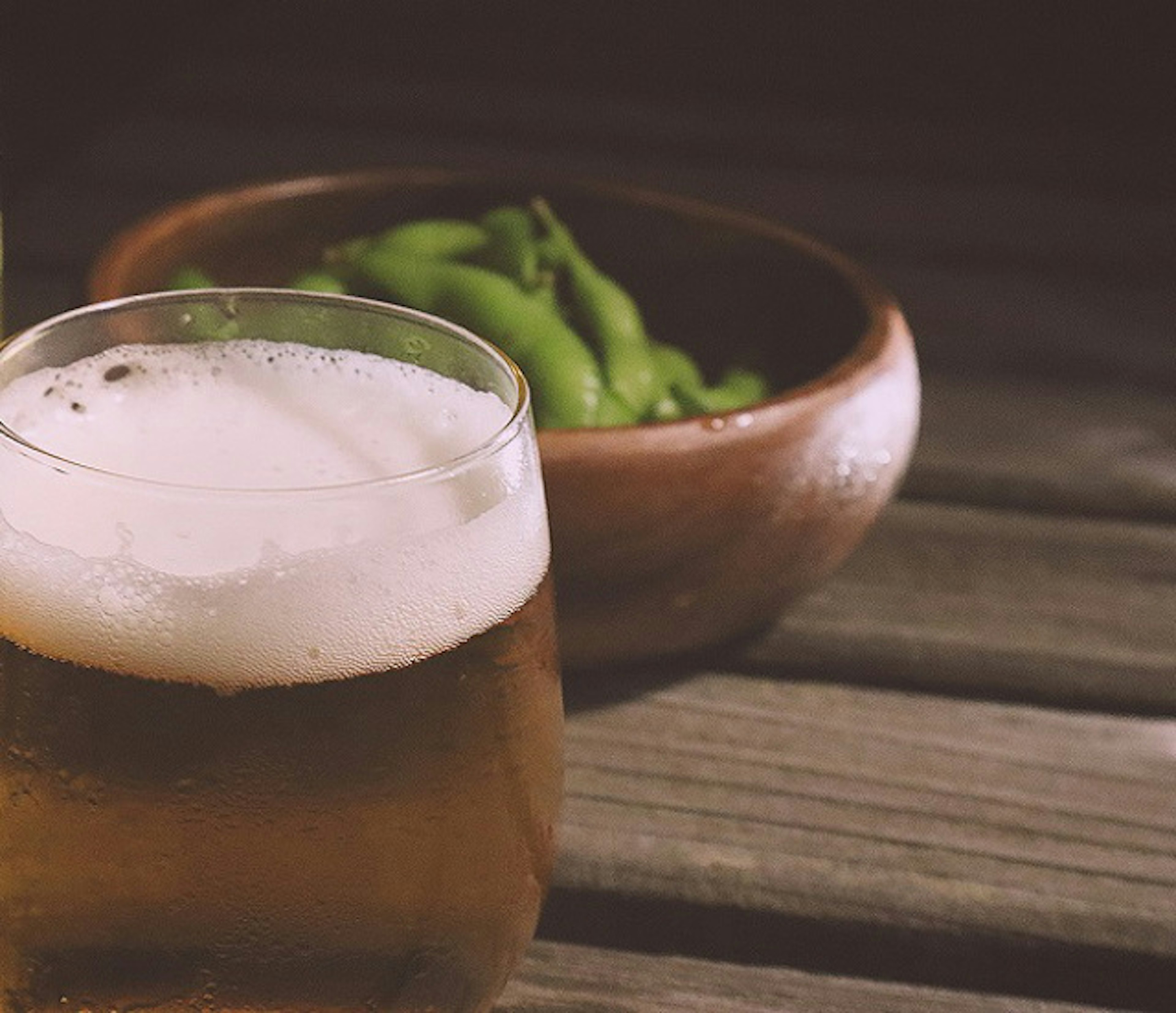 A scene with a glass of beer and a bowl of edamame on a wooden table