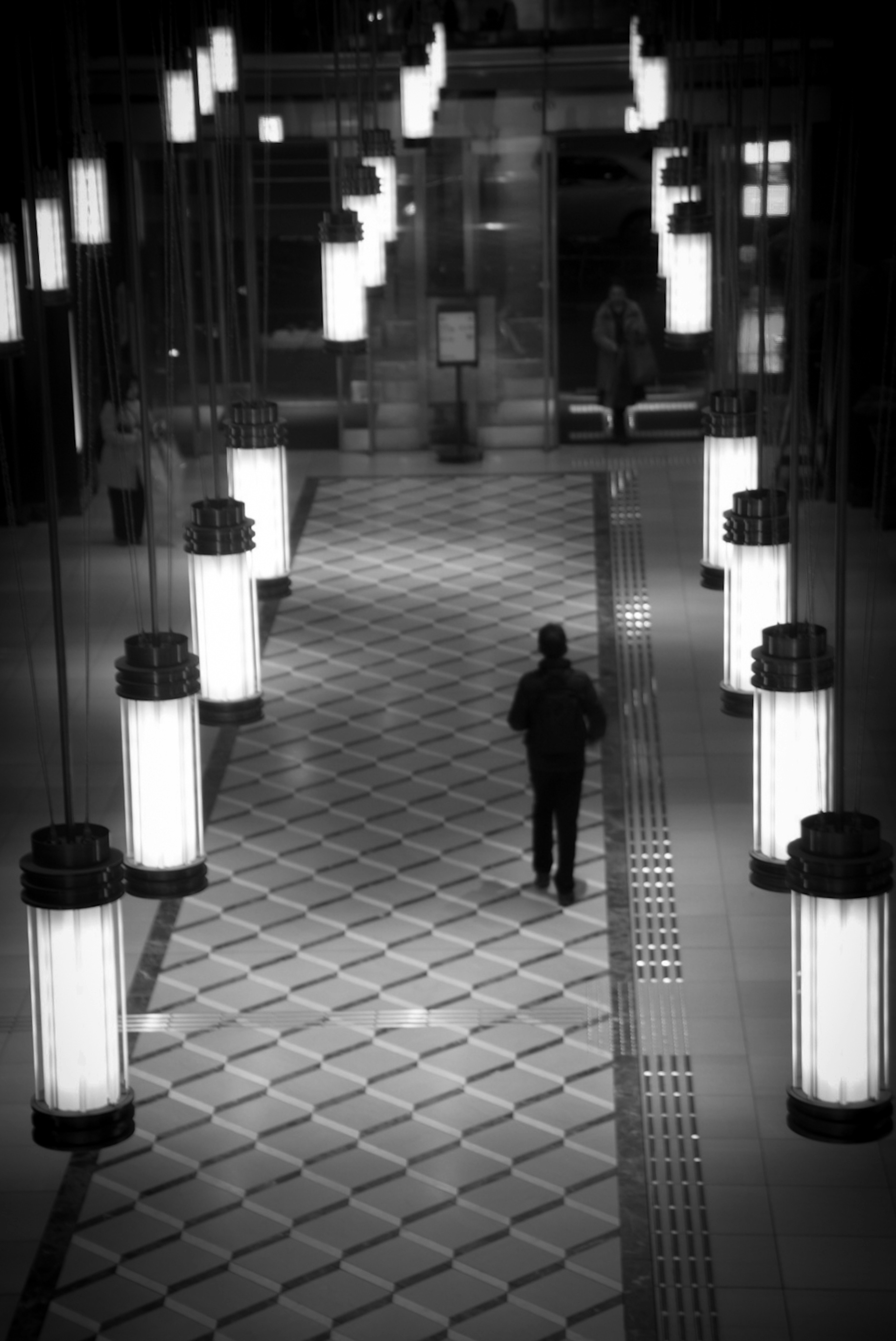 Una persona caminando en un pasillo en blanco y negro con lámparas brillantes