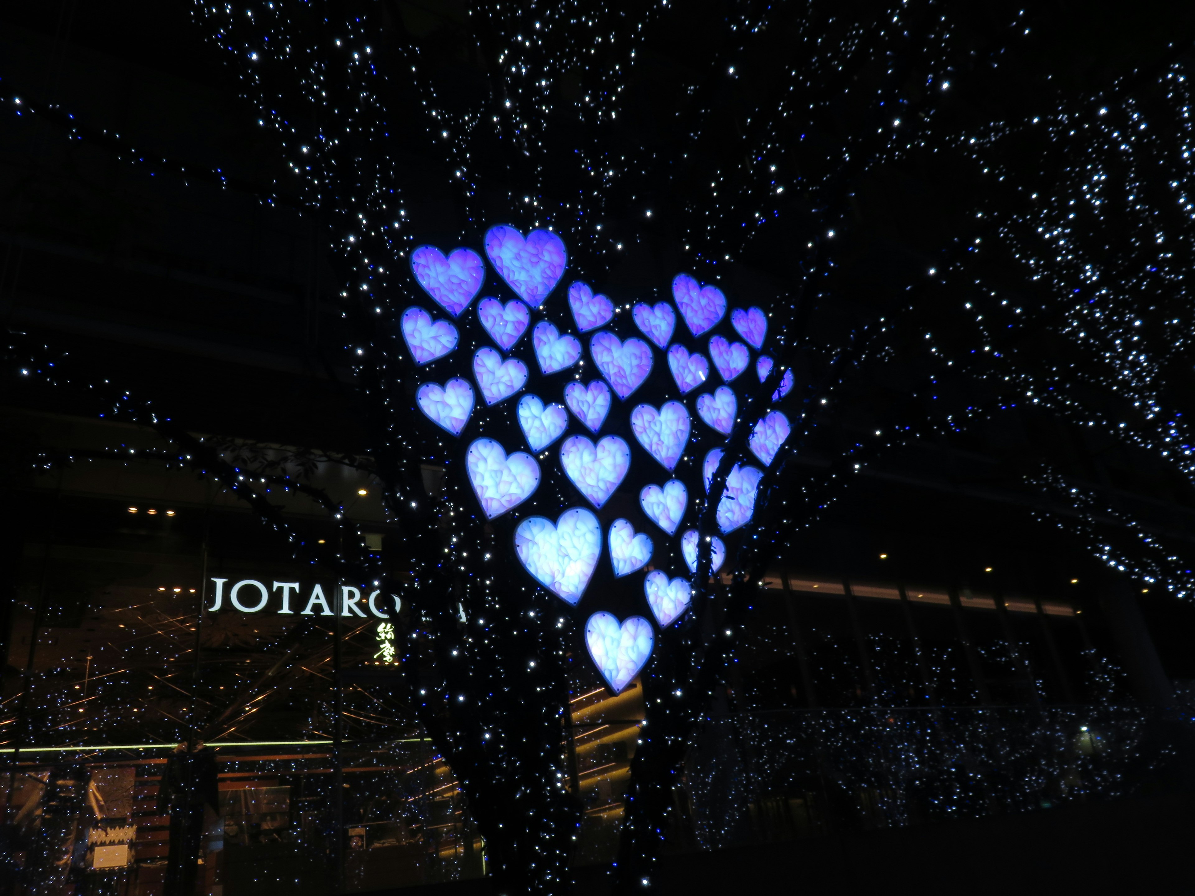 Albero adornato con luci a forma di cuore blu vicino a un'insegna