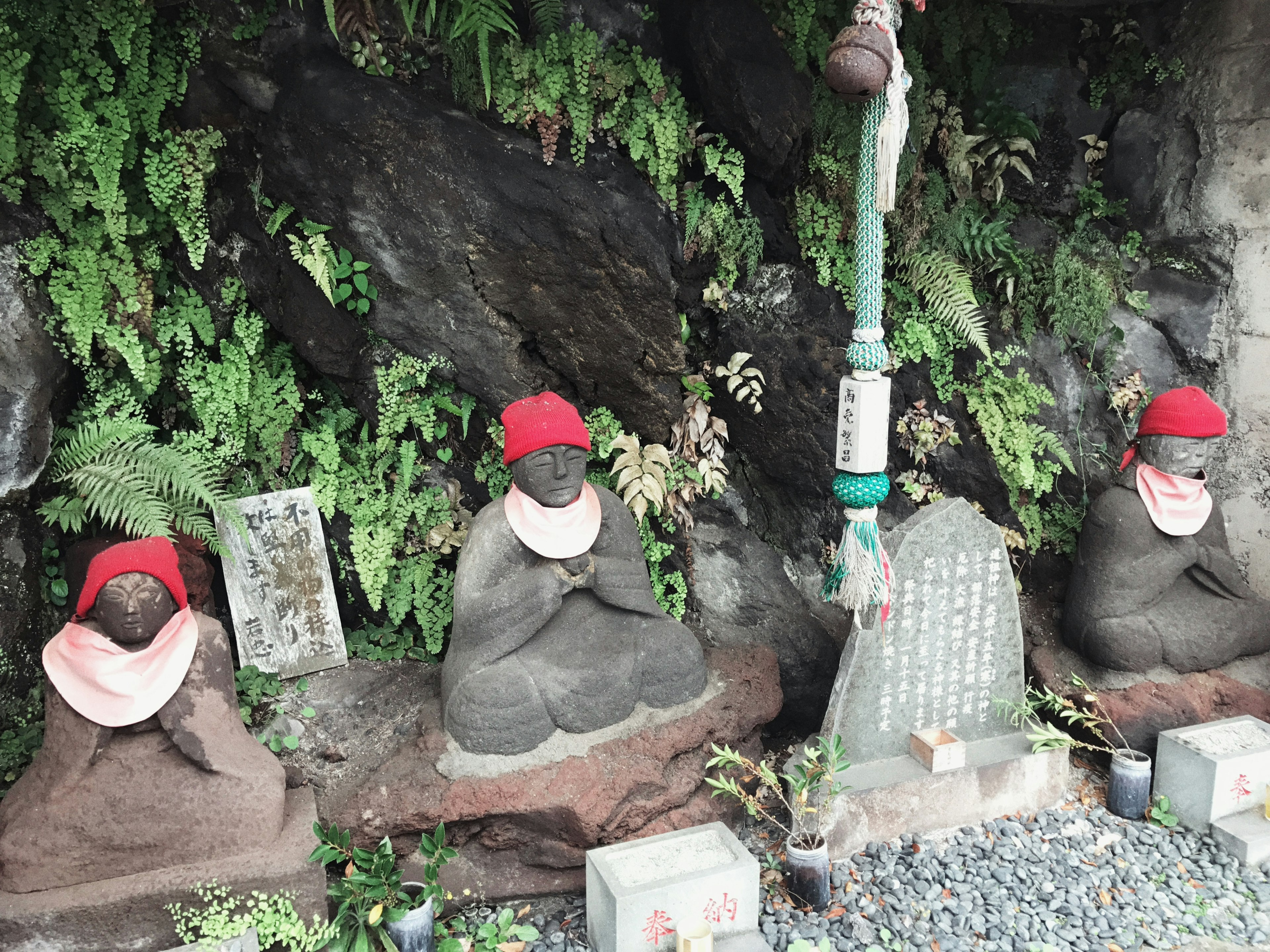 Stone statues wearing red hats set against a lush green background