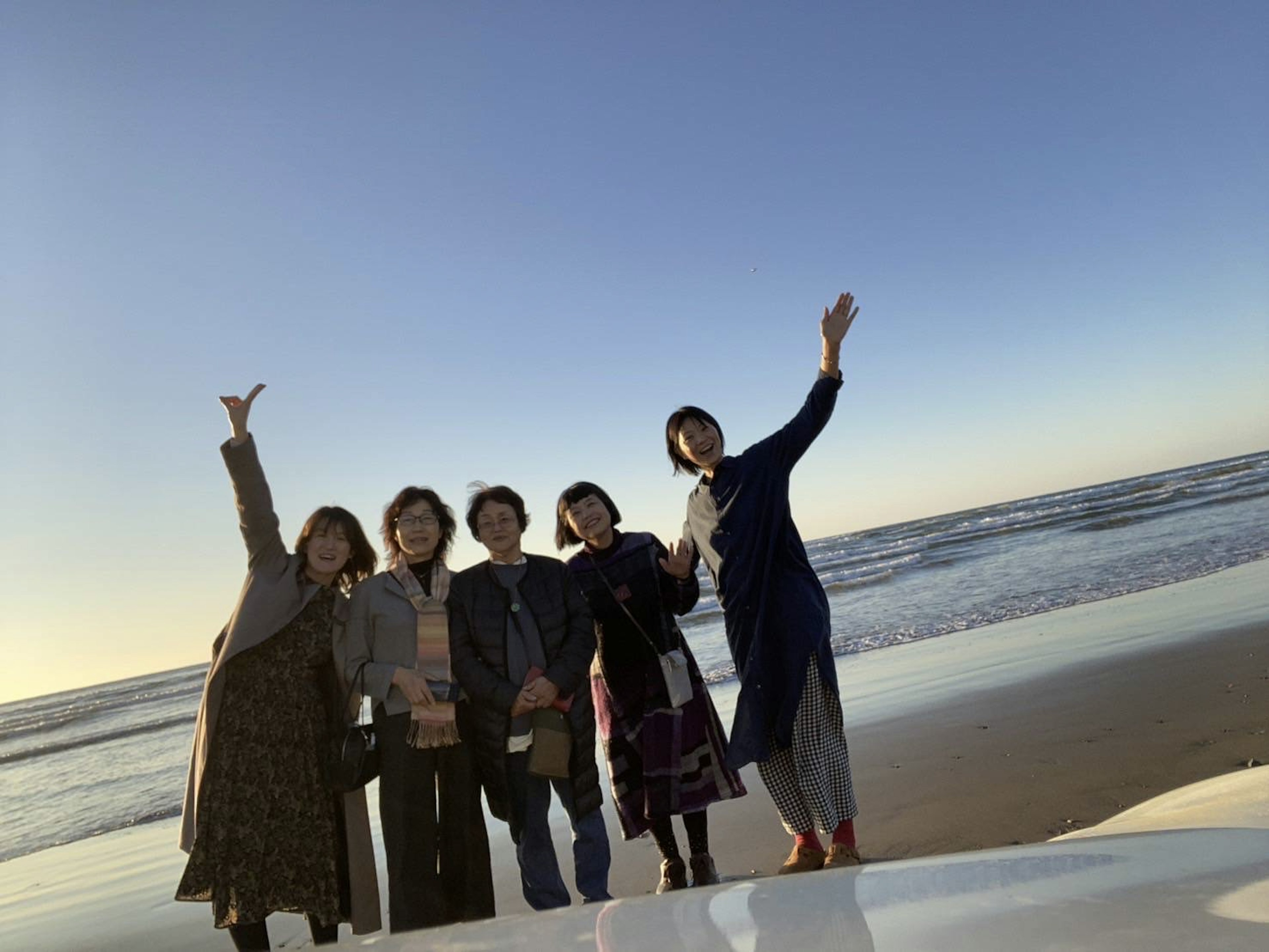 Sekelompok wanita berpose di pantai dengan langit biru dan ombak di latar belakang