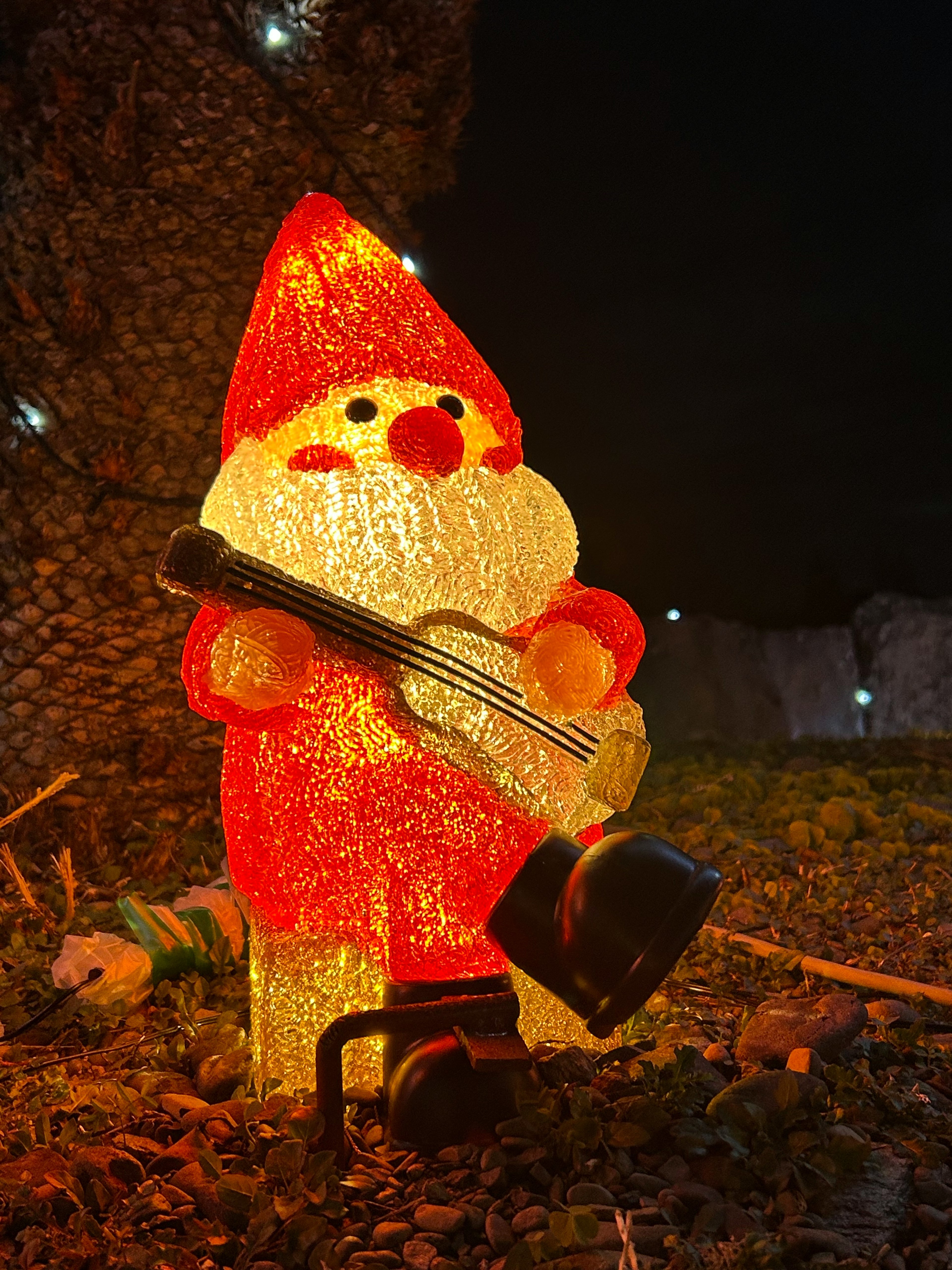 Illuminated Santa Claus holding a guitar in a nighttime setting