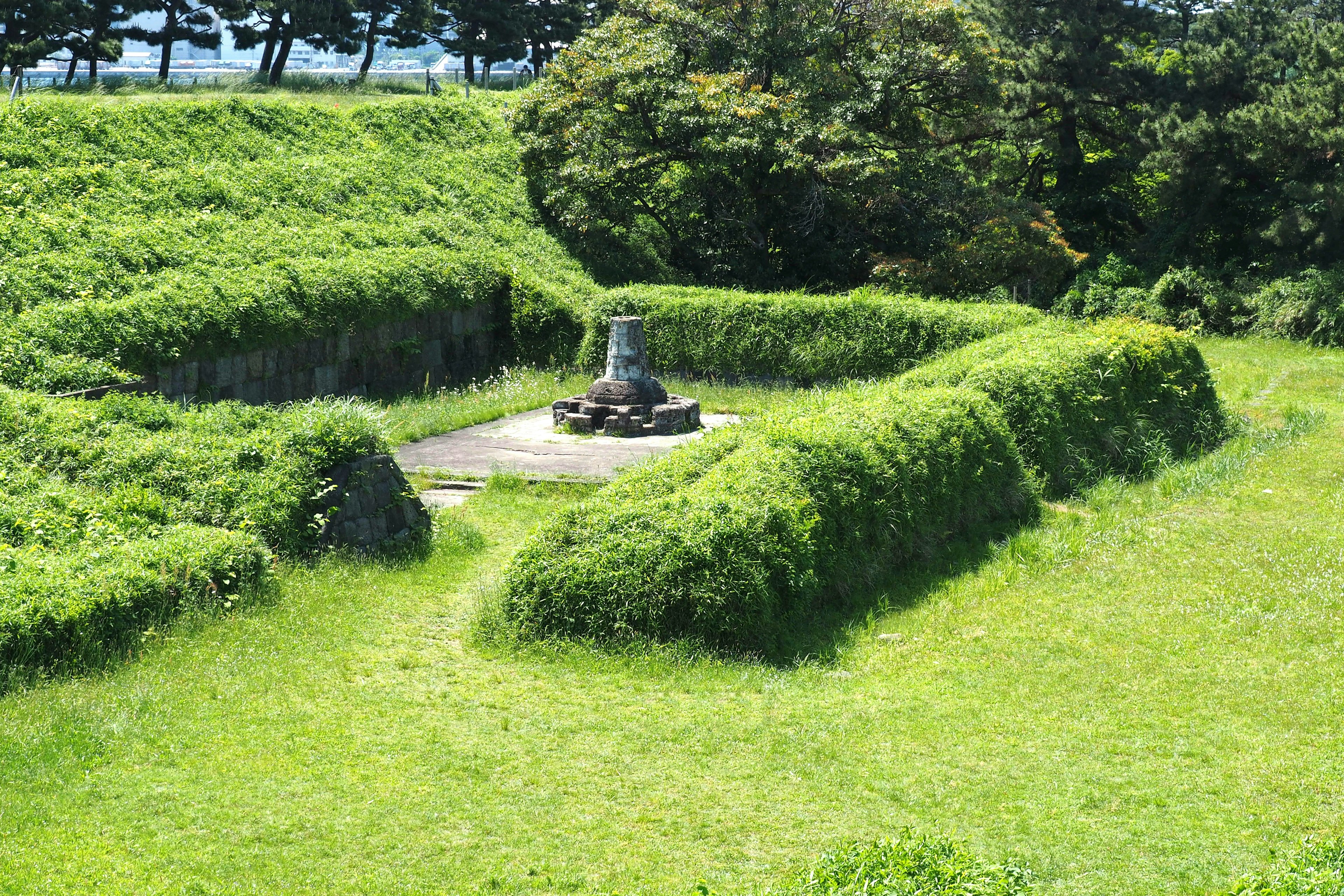 A small monument surrounded by lush greenery and hedges in a grassy area