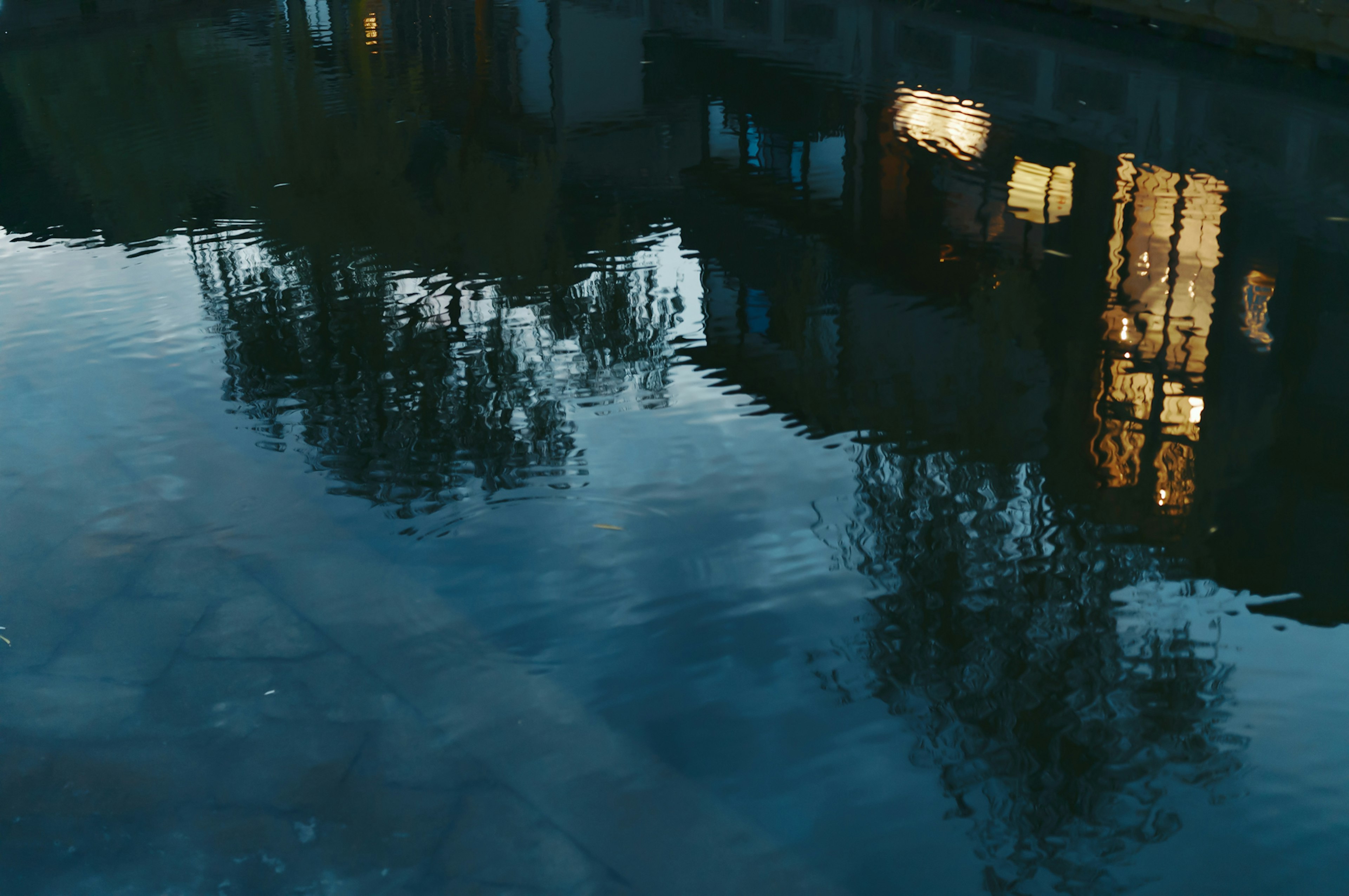 Calm water surface reflecting illuminated windows and tree shadows