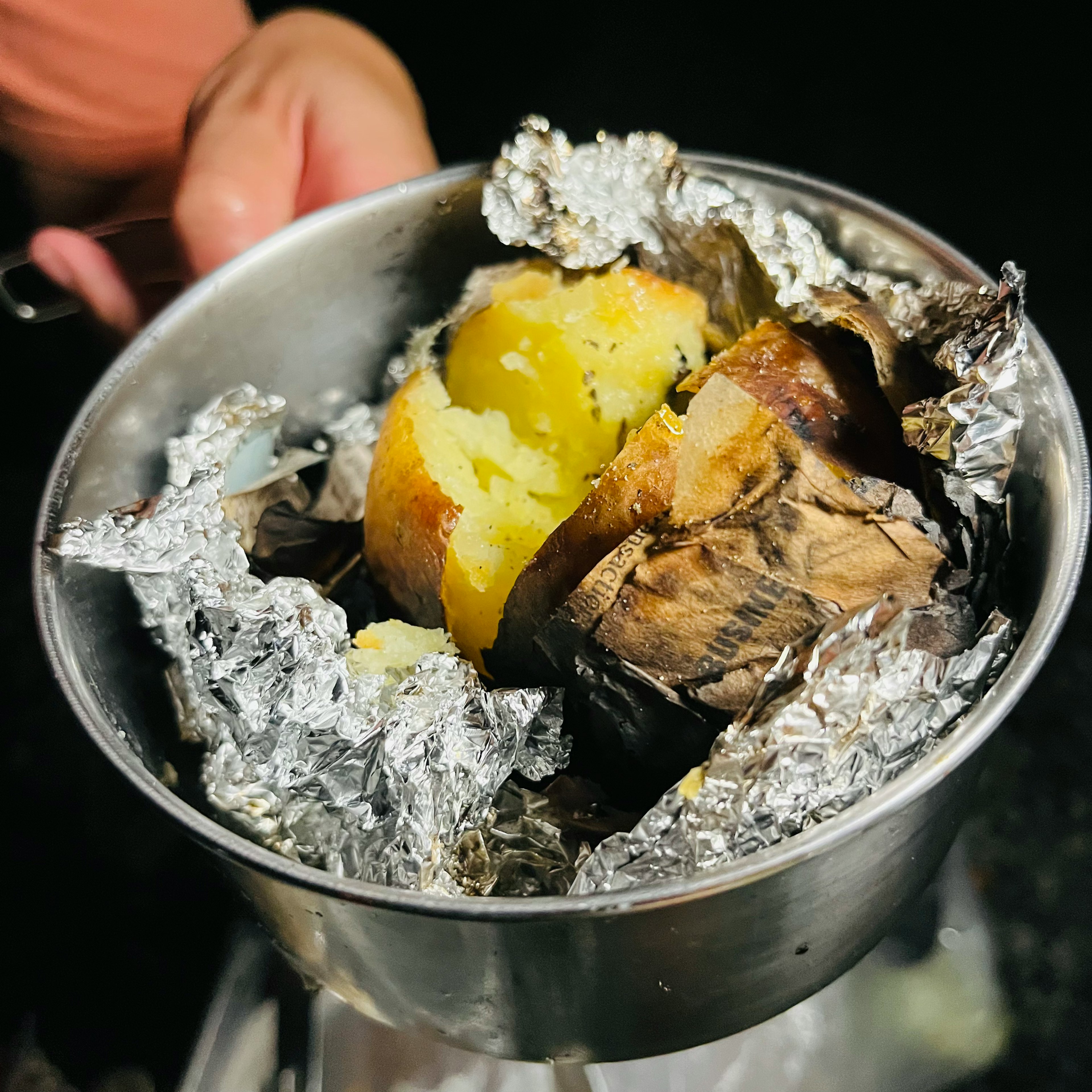 Una olla sostenida por una mano que contiene batatas horneadas envueltas en papel de aluminio