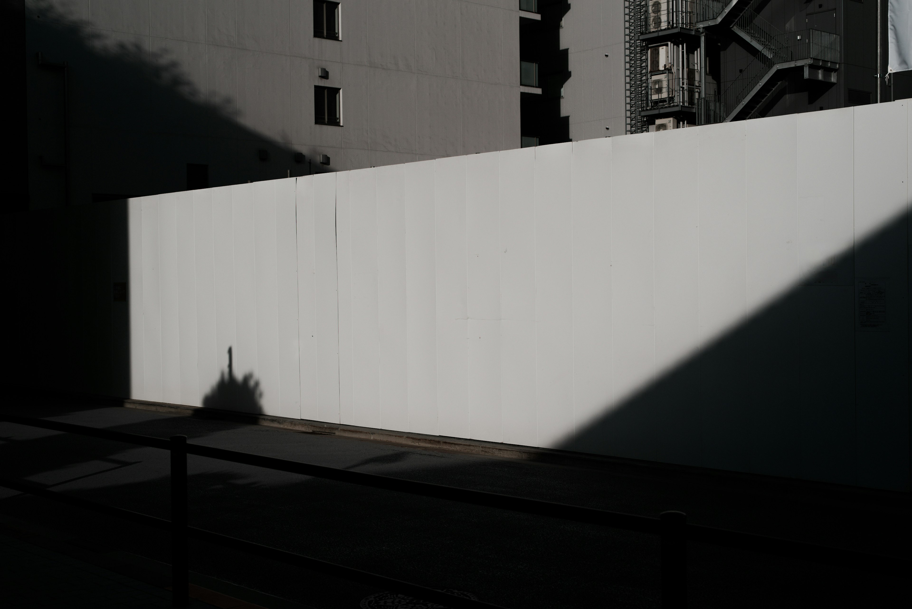 Urban scene featuring a stark white wall contrasted by shadows
