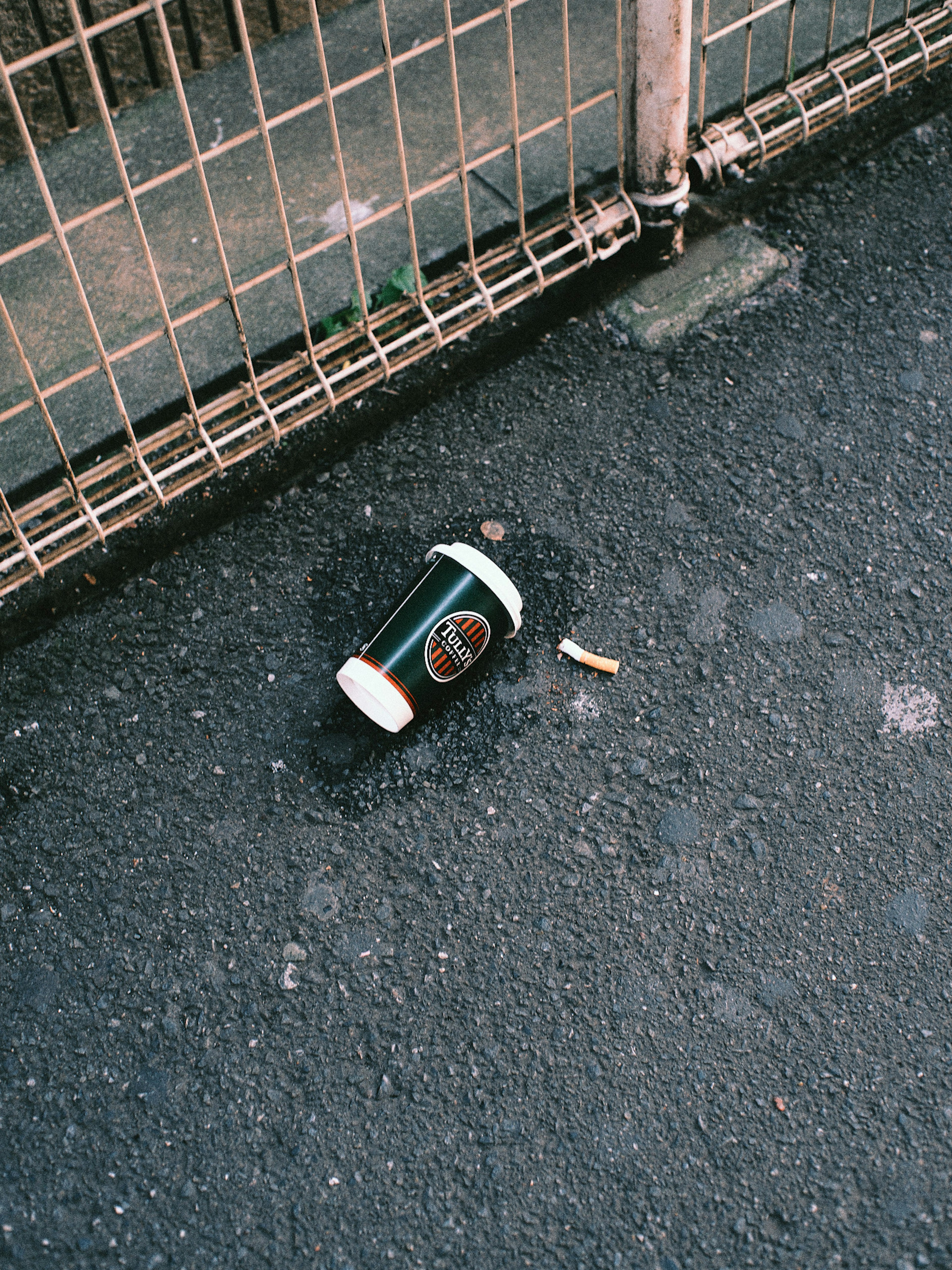 Un gobelet de café tombé et un mégot de cigarette sur le sol