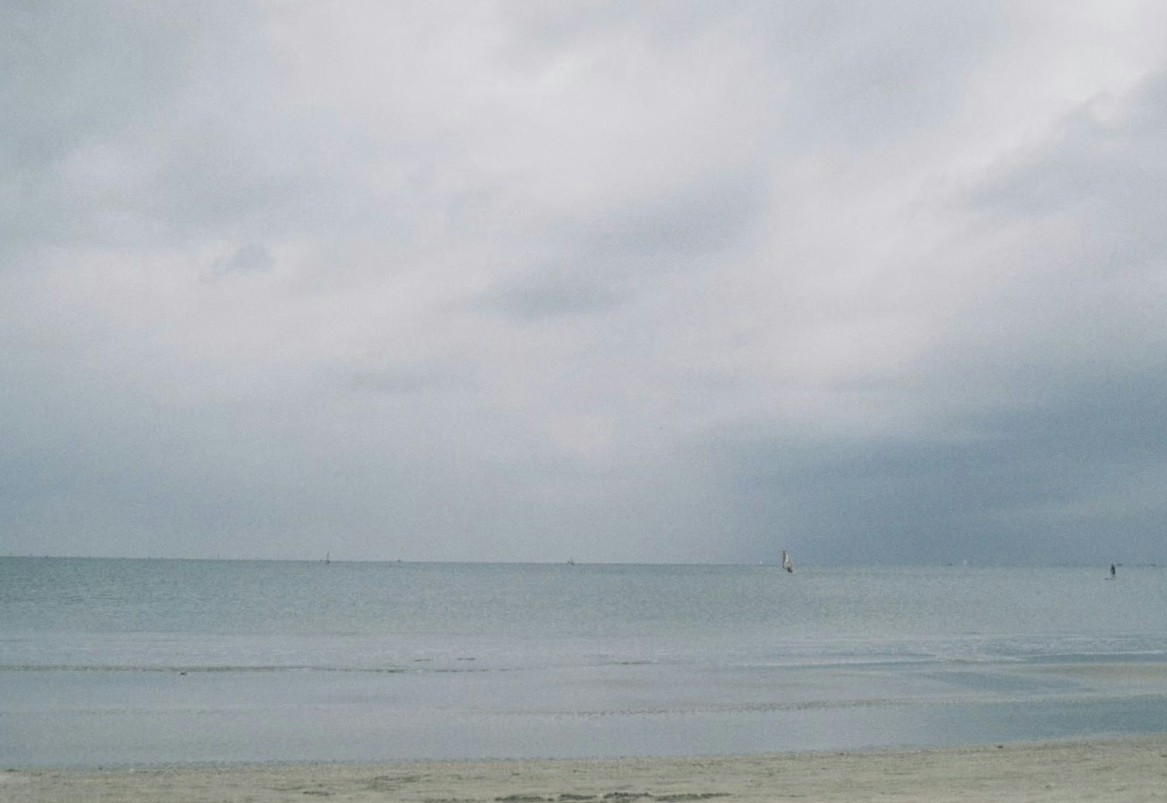 Langit mendung di atas laut tenang dengan pantai berpasir