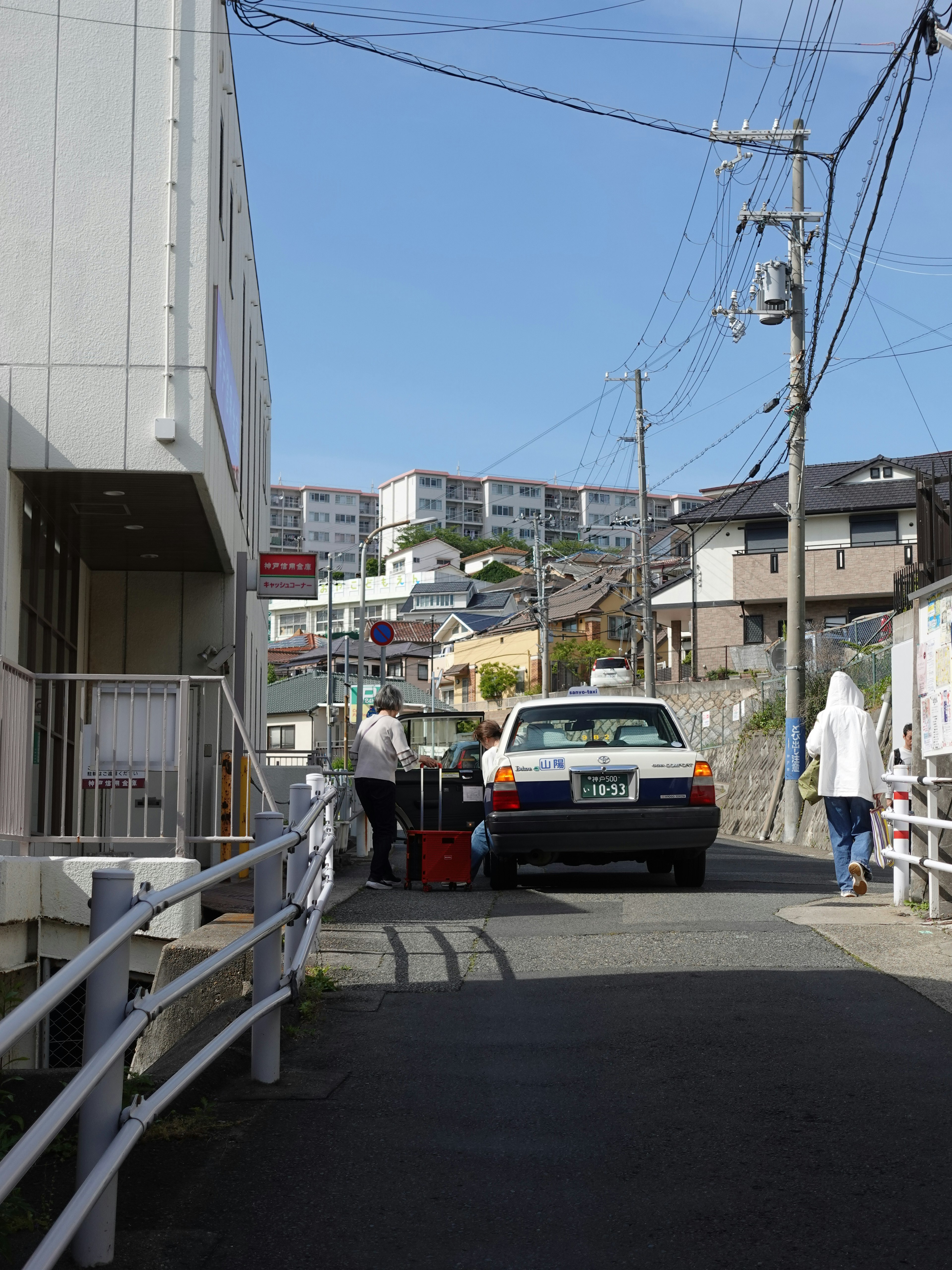 A taxi parked on a residential street with pedestrians walking on the sidewalk