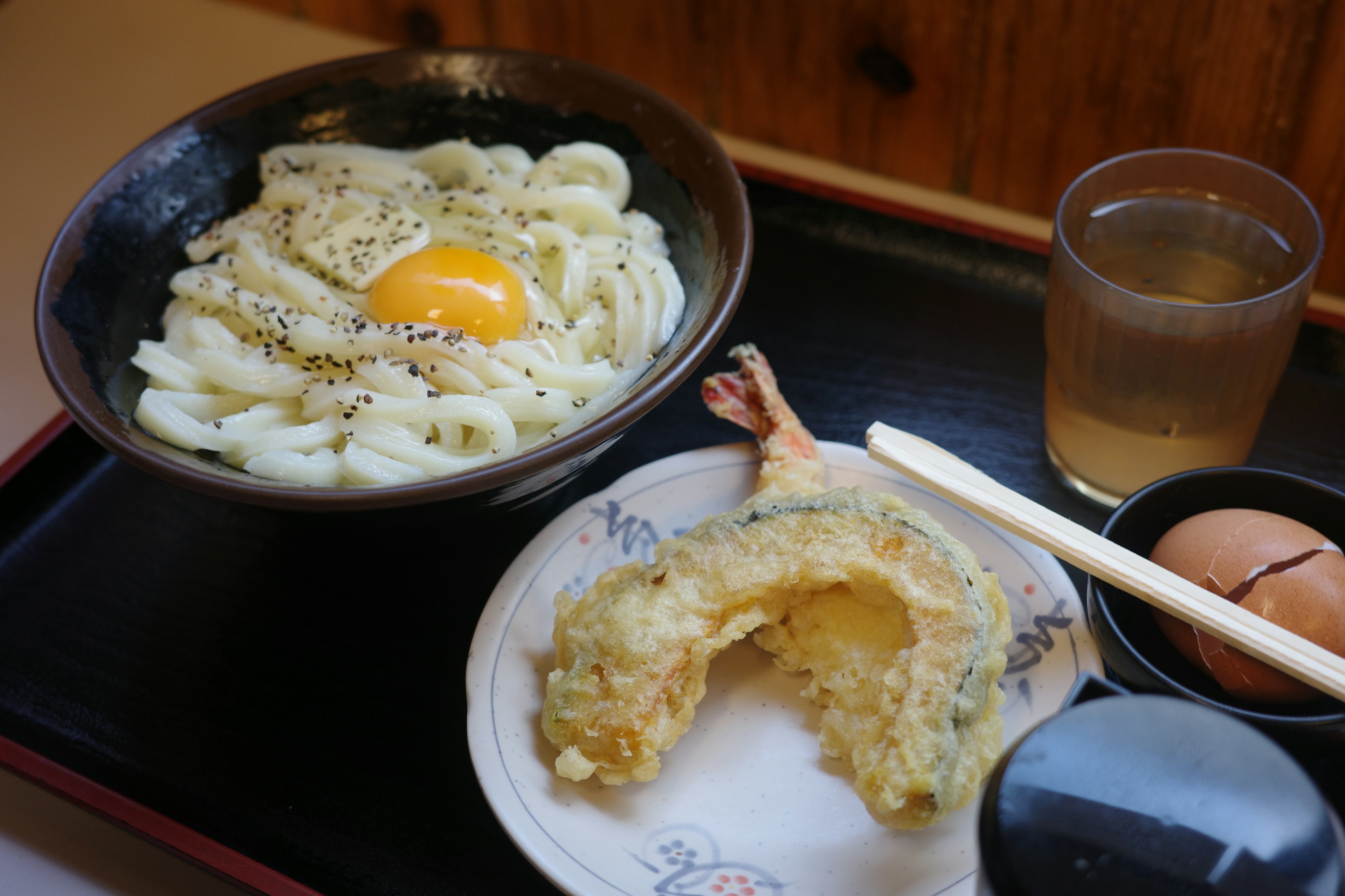 一碗乌冬面配鸡蛋和天妇罗，旁边有饮料