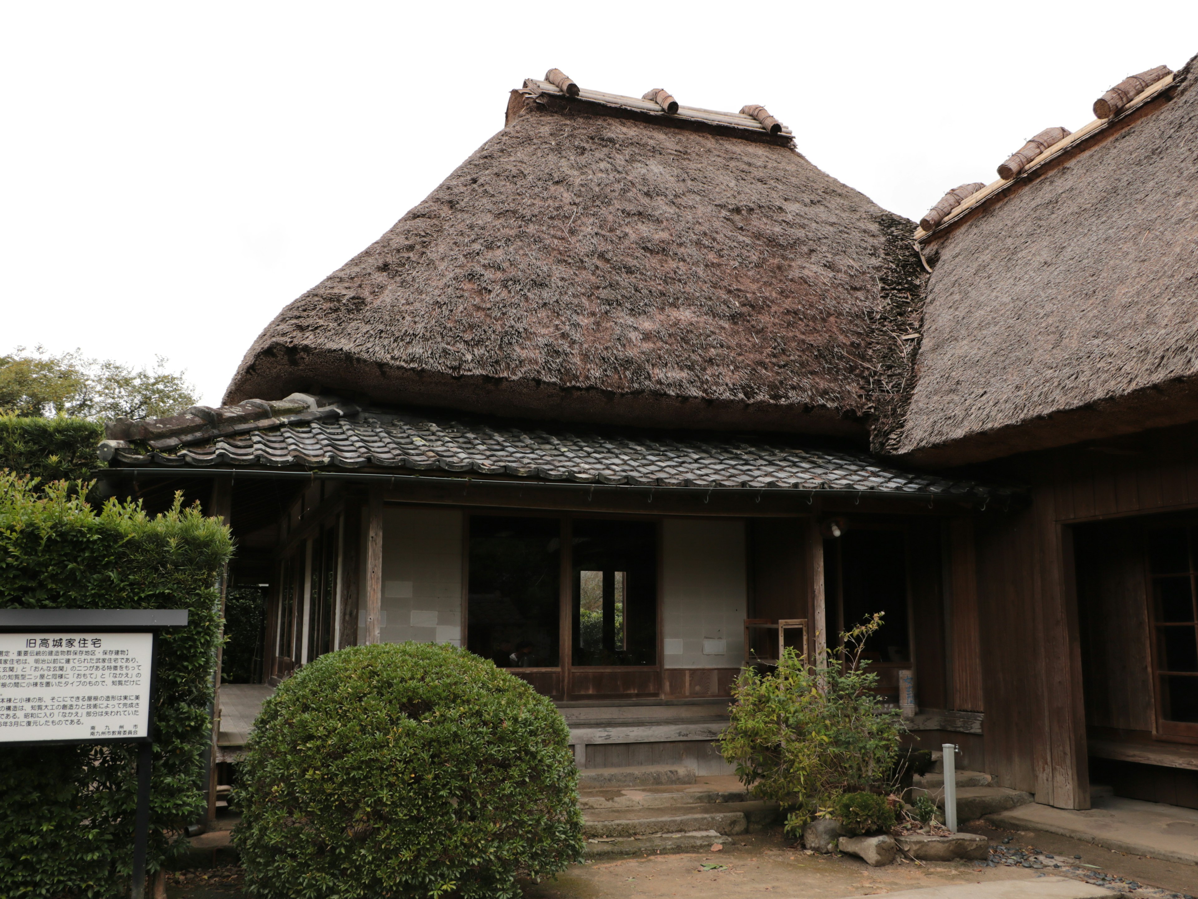 Extérieur d'une maison japonaise traditionnelle avec toit de chaume avec des plantes et un panneau visibles