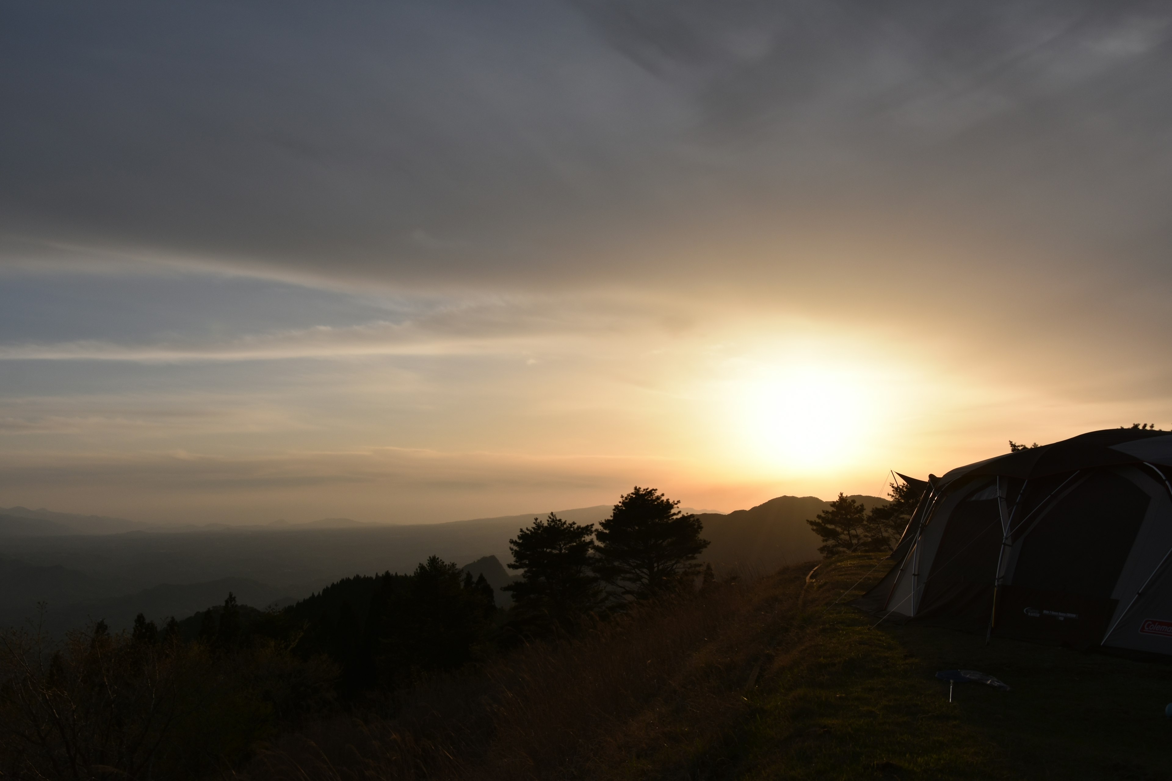 Matahari terbenam di lanskap pegunungan dengan tenda camping