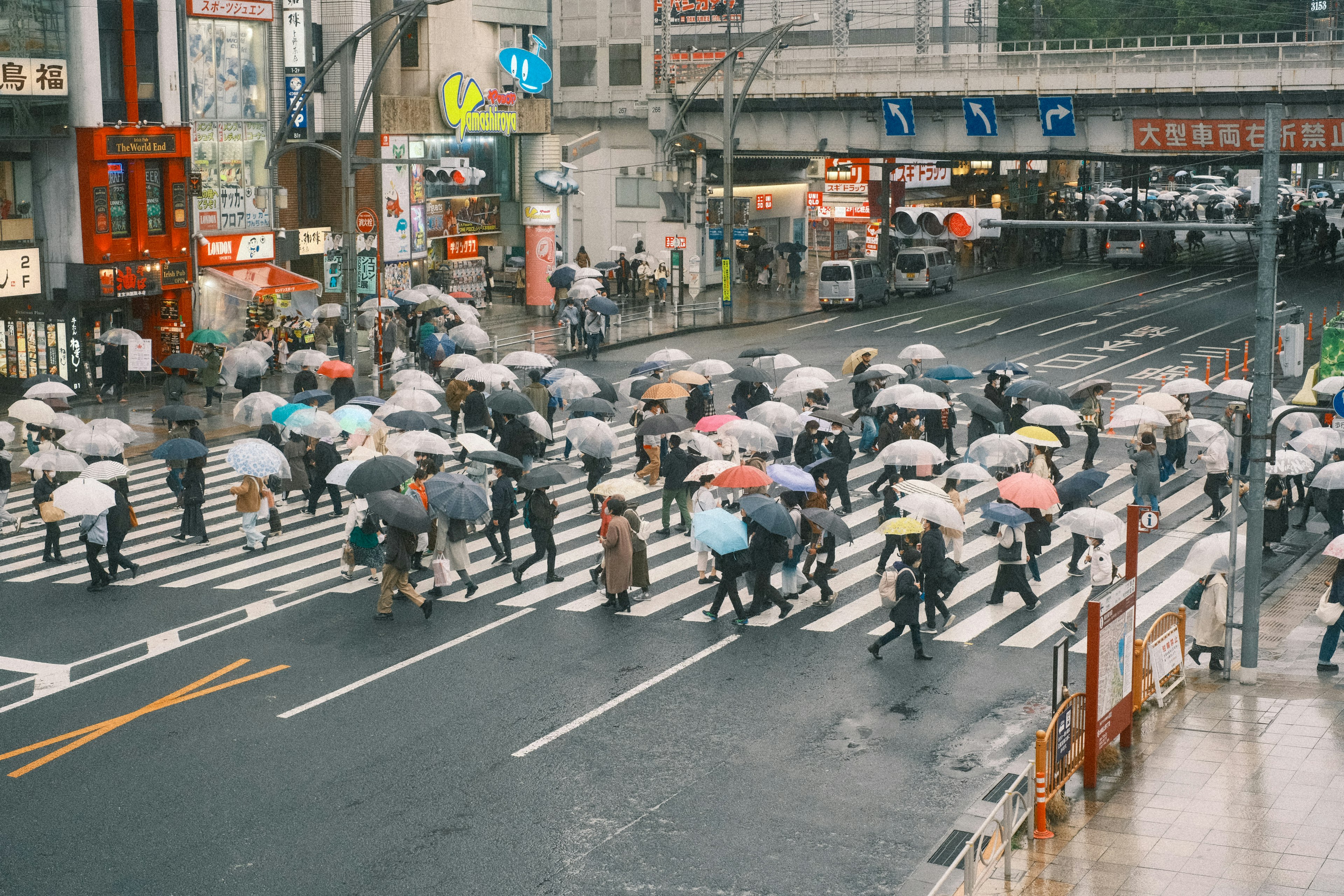 人々が傘をさして交差点を横断する場面の都市の風景