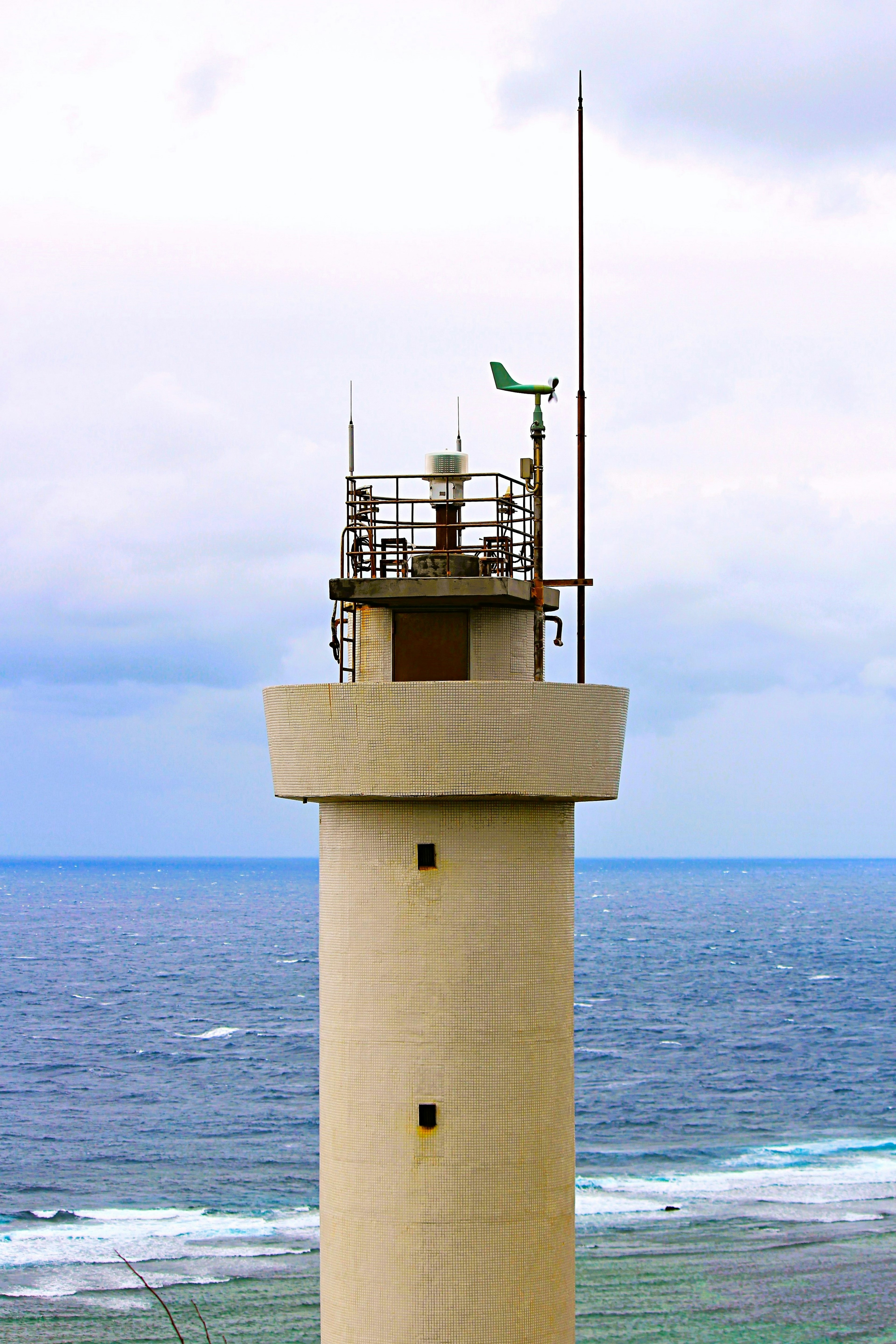 Un phare blanc avec un petit drapeau vert et une antenne de communication surplombant l'océan