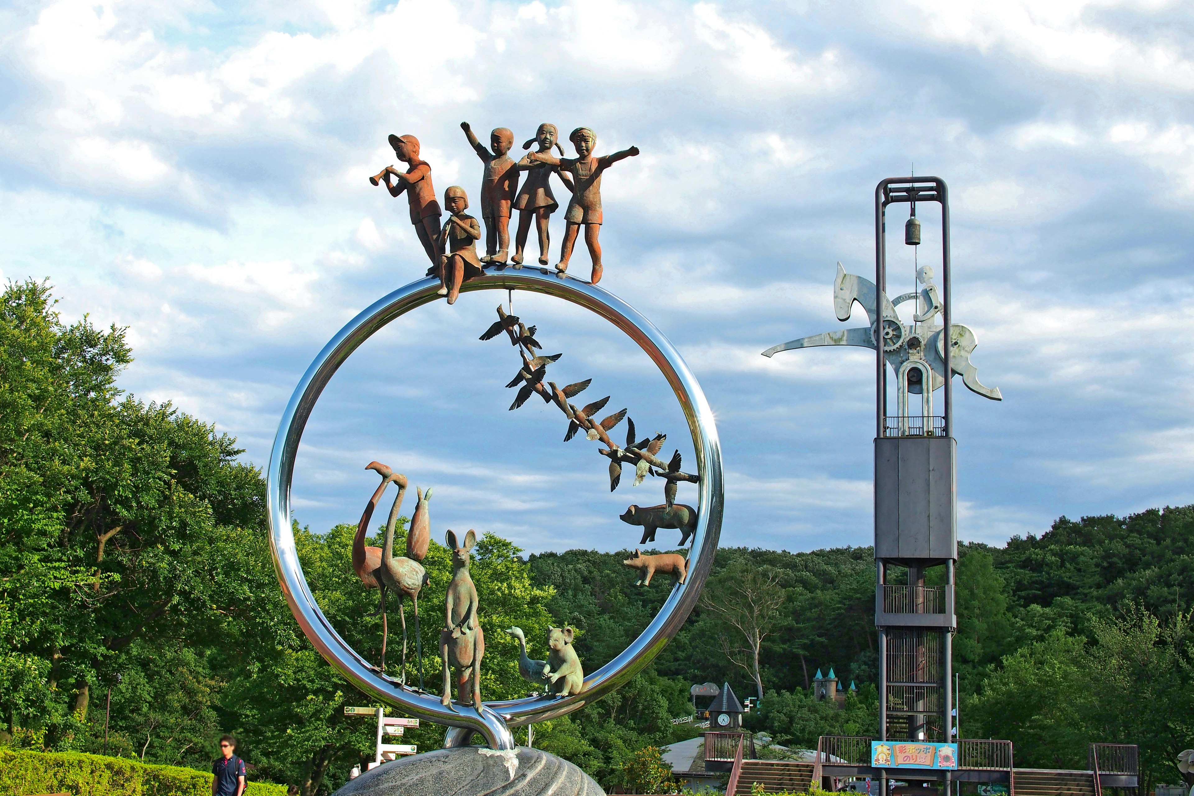 Sculpture of people standing on a circular frame with a wind turbine in the background